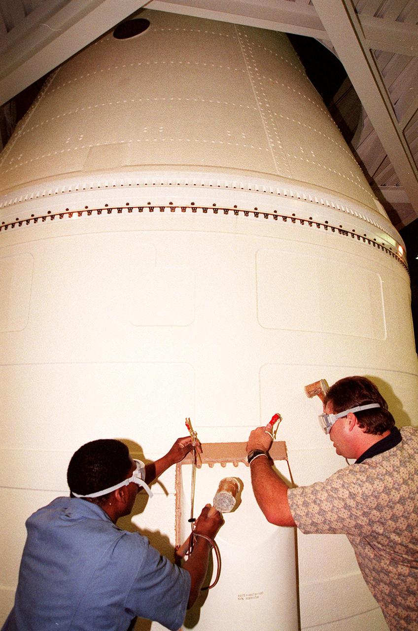 KENNEDY SPACE CENTER, FLA. -- In the Vehicle Assembly Building, near the top of the solid rocket booster, Henry Jones and Richard Bruns begin to detach the SRB system tunnel cover on the 36 cables inside. Jones and Bruns are United Space Alliance SRB technicians. The SRB is part of Space Shuttle Atlantis, rolled back from Launch Pad 39A in order to conduct tests on the cables. A prior extensive evaluation of NASA’s SRB cable inventory on the shelf revealed conductor damage in four (of about 200) cables. Shuttle managers decided to prove the integrity of the system tunnel cables already on Atlantis before launching. Workers are conducting inspections, making continuity checks and conducting X-ray analysis on the cables. The launch has been rescheduled no earlier than Feb. 6.<br