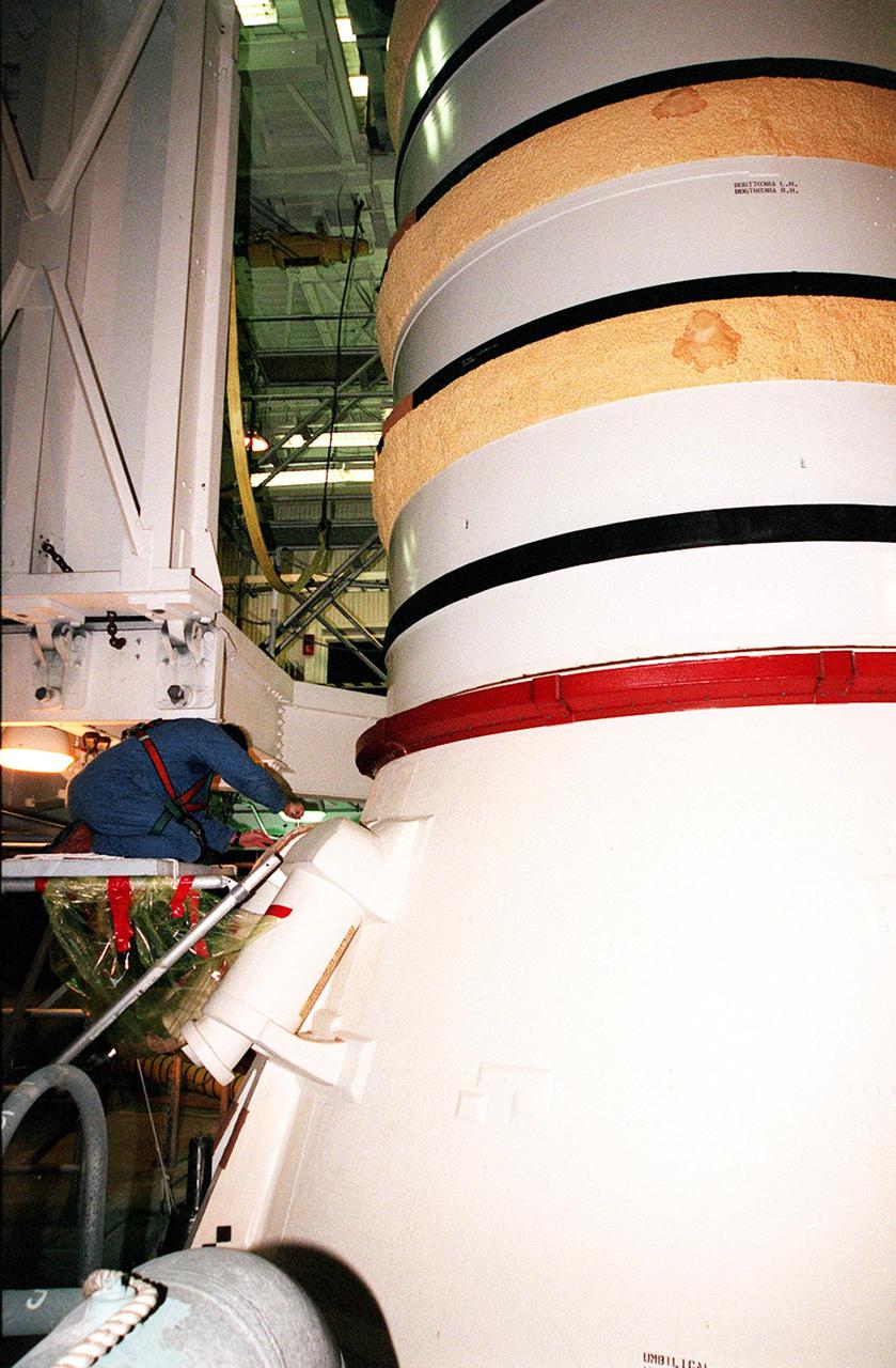 KENNEDY SPACE CENTER, FLA. -- Near the bottom of the solid rocket booster, a worker in the Vehicle Assembly Building begins to detach the SRB system tunnel cover on the 36 cables inside. The SRB is part of Space Shuttle Atlantis, rolled back from Launch Pad 39A in order to conduct tests on the cables. A prior extensive evaluation of NASA’s SRB cable inventory on the shelf revealed conductor damage in four (of about 200) cables. Shuttle managers decided to prove the integrity of the system tunnel cables already on Atlantis before launching. Workers are conducting inspections, making continuity checks and conducting X-ray analysis on the cables. The launch has been rescheduled no earlier than Feb. 6. <br