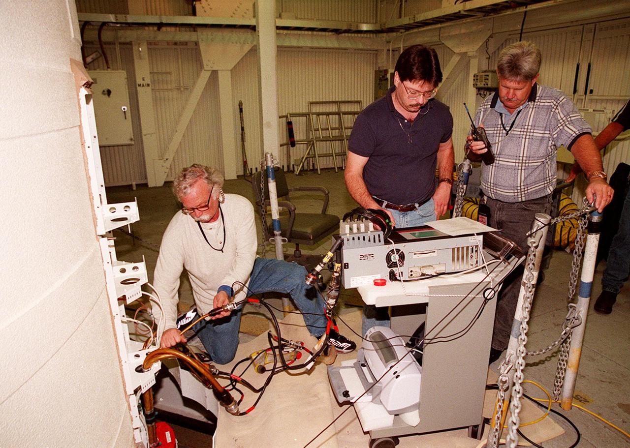 KENNEDY SPACE CENTER, FLA. -- Working near the top of a solid rocket booster, NASA and United Space Alliance SRB technicians hook up SRB cables to a CIRRUS computer for testing. From left are Jim Glass, with USA, performing a Flex test on the cable; Steve Swichkow, with NASA, and Jim Silviano, with USA, check the results on a computer. The SRB is part of Space Shuttle Atlantis, rolled back from Launch Pad 39A in order to conduct tests on the cables. A prior extensive evaluation of NASA’s SRB cable inventory on the shelf revealed conductor damage in four (of about 200) cables. Shuttle managers decided to prove the integrity of the system tunnel cables already on Atlantis before launching. Workers are conducting inspections, making continuity checks and conducting X-ray analysis on the cables. The launch has been rescheduled no earlier than Feb. 6. <br