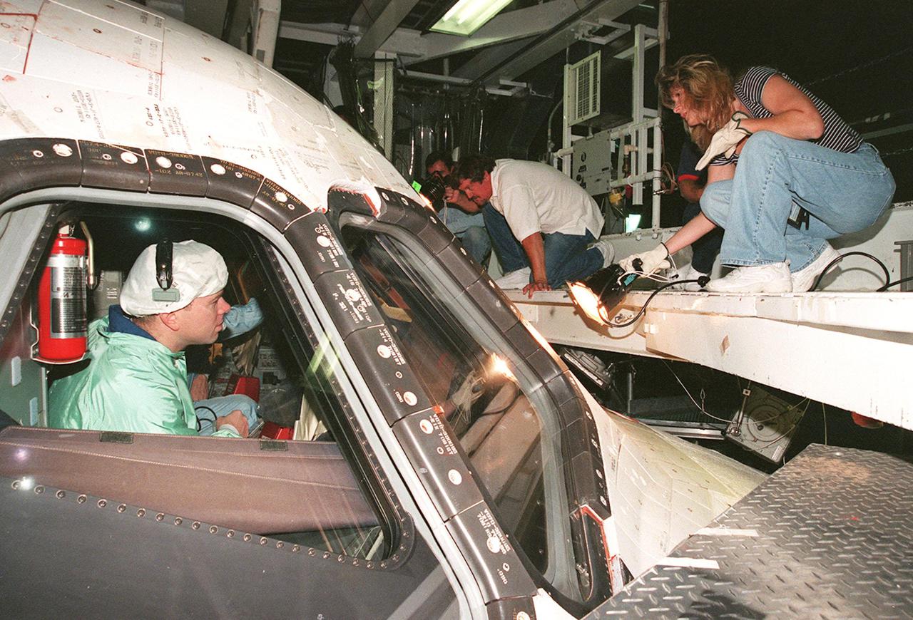 In the Orbiter Processing Facility bay 1, STS-102 Pilot James W. Kelly checks out the window of Discovery from the inside while workers (right) check the outside. The mission crew is at KSC for Crew Equipment Interface Test activities.