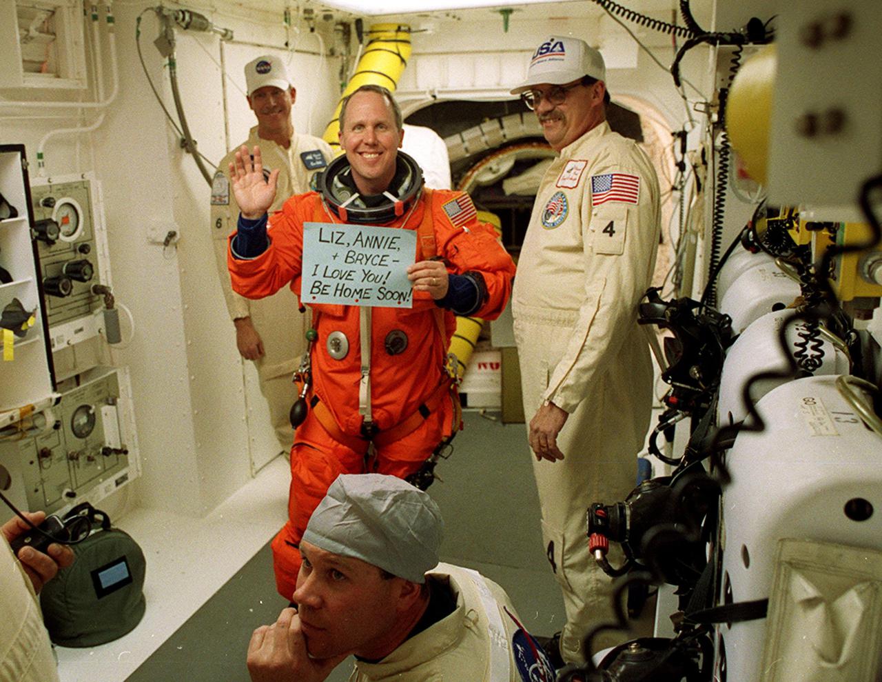 In the White Room with the closeout crew, STS-98 Mission Specialist Thomas Jones shows a message to his family before he enters Space Shuttle Atlantis for launch. The White Room is an environmentally controlled room at the end of the Orbiter Access Arm. Atlantis is carrying the U.S. Laboratory Destiny, a key module in the growth of the Space Station. Destiny will be attached to the Unity node on the Space Station using the Shuttle’s robotic arm. Three spacewalks are required to complete the planned construction work during the 11-day mission. This mission marks the seventh Shuttle flight to the Space Station, the 23rd flight of Atlantis and the 102nd flight overall in NASA’s Space Shuttle program. The planned landing is at KSC Feb. 18 about 1 p.m