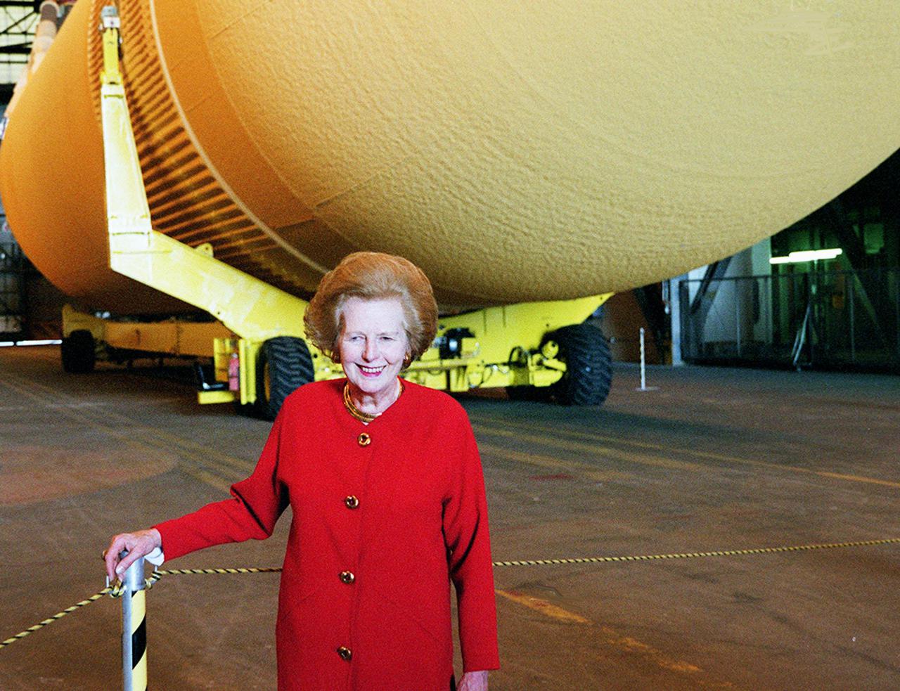 An optical illusion places Lady Margaret Thatcher, former Prime Minister of Great Britain, under an external tank in the Vehicle Assembly Building. In reality, the ET is behind her, waiting in the transfer aisle for stacking on the next Shuttle. Lady Thatcher is touring KSC