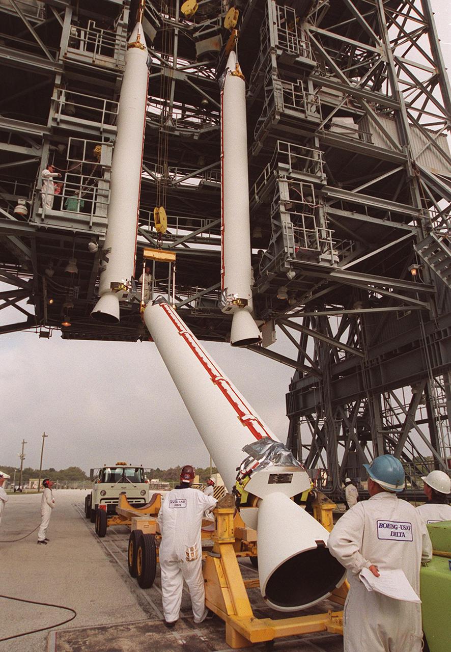 Workers on Launch Pad 17-A, Cape Canaveral Air Force Station, keep watch as a solid rocket booster is lifted in between two other SRBs suspended from the gantry. They will be mated with a Delta 7925 rocket for launch April 7, 2001. The rocket will carry the 2001 Mars Odyssey Orbiter, containing three science instruments: THEMIS, the Gamma Ray Spectrometer (GRS), and the Mars Radiation Environment Experiment (MARIE). THEMIS will map the mineralogy and morphology of the Martian surface using a high-resolution camera and a thermal infrared imaging spectrometer. The GRS will achieve global mapping of the elemental composition of the surface and determine the abundance of hydrogen in the shallow subsurface. The MARIE will characterize aspects of the near-space radiation environment with regards to the radiation-related risk to human explorers