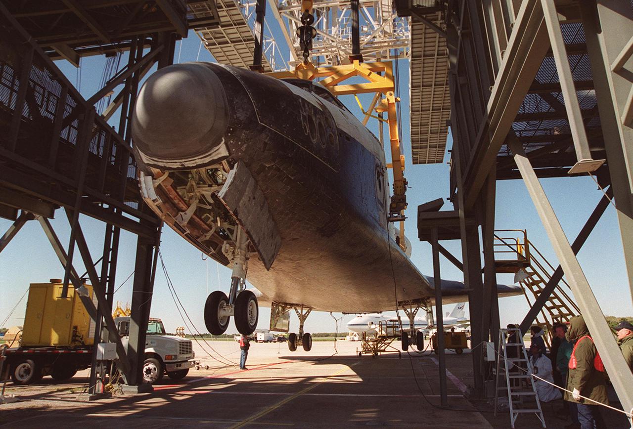 The wheels on Atlantis are lowered while the orbiter is suspended by an overhead crane in the mate_demate device at KSC’s Shuttle Landing Facility. It was removed from the back of the Shuttle Carrier Aircraft in the background. Atlantis just returned from California atop the SCA after its Feb. 19 landing at Edwards Air Force Base concluding mission STS-98. The ferry flight began March 1; unfavorable weather conditions kept it on the ground at Altus AFB, Okla., until it could return to Florida. Atlantis will be transported to the Orbiter Processing Facility to prepare it for mission STS-104, the 10th construction flight to the International Space Station, scheduled to launch June 8