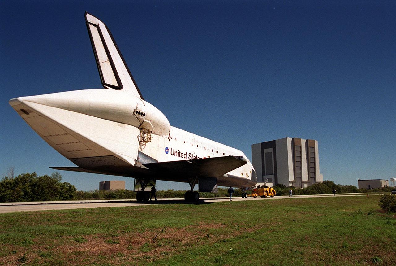 Towed from the Shuttle Landing Facility, Atlantis heads for the Orbiter Processing Facility (far right). The large building is the Vehicle Assembly Building, where orbiters are mated to their solid rocket booster-external tank stack prior to rollout to the launch pad. In view is the tail cone that orbiters use when being carried piggyback on ferry flights atop a Shuttle Carrier Aircraft. The tail cone protects the aft engine area and provides a more efficient aeronautical dimension during flight. Atlantis returned from California atop a Shuttle Carrier Aircraft after its Feb. 19 landing at Edwards Air Force Base, concluding mission STS-98. The ferry flight began March 1; unfavorable weather conditions kept it on the ground at Altus AFB, Okla., until it could return to Florida. In the Orbiter Processing Facility, Atlantis will be prepared for mission STS-104, the 10th construction flight to the International Space Station, scheduled to launch June 8