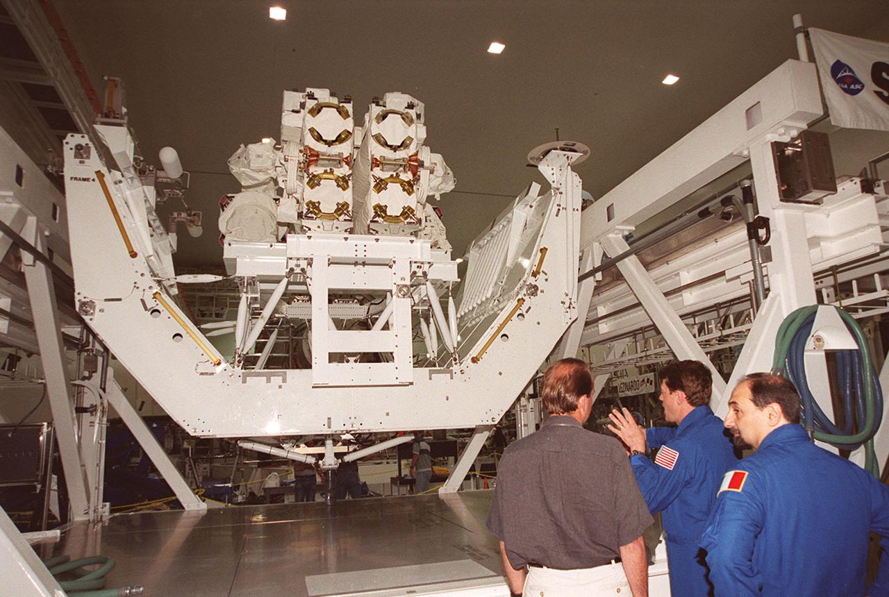 KSC’s PAO videographer, Glenn Benson (left) listens to STS-100 Pilot Jeffrey S. Ashby explain use of the Canadian robotic arm, SSRMS (left), in the Space Station Processing Facility. At right is Mission Specialist Umberto Guidoni. The STS-100 crew is at KSC for Terminal Countdown Demonstration Test activities that include emergency escape training at the pad and a simulated launch countdown. The mission is carrying the Multi-Purpose Logistics Module Raffaello and the SSRMS, to the International Space Station. Raffaello carries six system racks and two storage racks for the U.S. Lab. The SSRMS is crucial to the continued assembly of the orbiting complex. Launch of mission STS-100 is scheduled for April 19 at 2:41 p.m. EDT from Launch Pad 39A