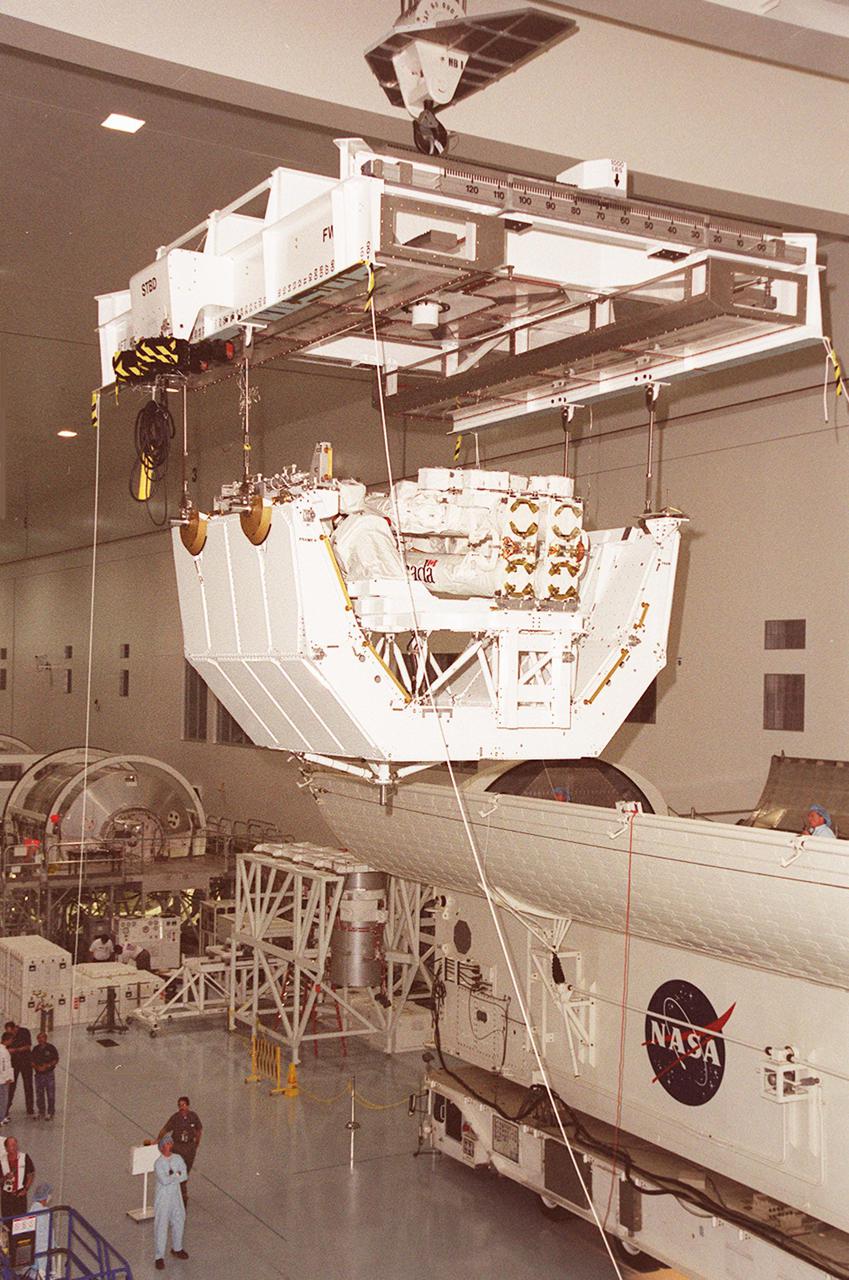 In the Space Station Processing Facility, the overhead crane rolls along the ceiling with the pallet and Canadian robotic arm, SSRMS, toward the payload canister, at right. The arm is 57.7 feet (17.6 meters) long when fully extended and has seven motorized joints. It is capable of handling large payloads and assisting with docking the Space Shuttle. The SSRMS is self-relocatable with a Latching End Effector, so it can be attached to complementary ports spread throughout the Station’s exterior surfaces. The SSRMS is part of the payload on mission STS-100, scheduled to launch April 19 at 2:41 p.m. EDT from Launch Pad 39A, KSC