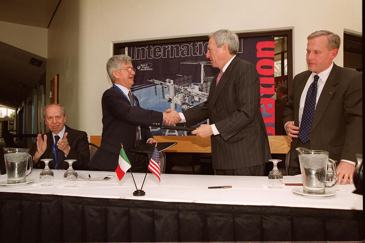 After signing a Framework for Cooperation to build the Habitation Module for the International Space Station, Italian Space Agency President Sergio DeJulio (standing, left) shakes hands with NASA Administrator Daniel S. Goldin (right). Also at the signing are The Honorable Lamberto Dini, Minister of Foreign Affairs, Republic of Italy (far left) and John Schumacher, assistant administrator, NASA External Relations. The Framework is a potential bilateral cooperative agreement that could result in ASI development of a U.S. Habitation Module for the International Space Station. This agreement allows the U.S. to explore an alternative approach to achieve full crew habitation for the ISS. A Memorandum of Understanding (MOU) between NASA and ASI will be required to formally document NASA and ASI’s respective responsibilities in a legally binding document. The Framework signed today would form the basis for a potential MOU which NASA and ASI would sign after completion of the program assessment and subsequent negotiations.The ceremony took place at the IMAX Theater, Kennedy Space Center Visitor Complex