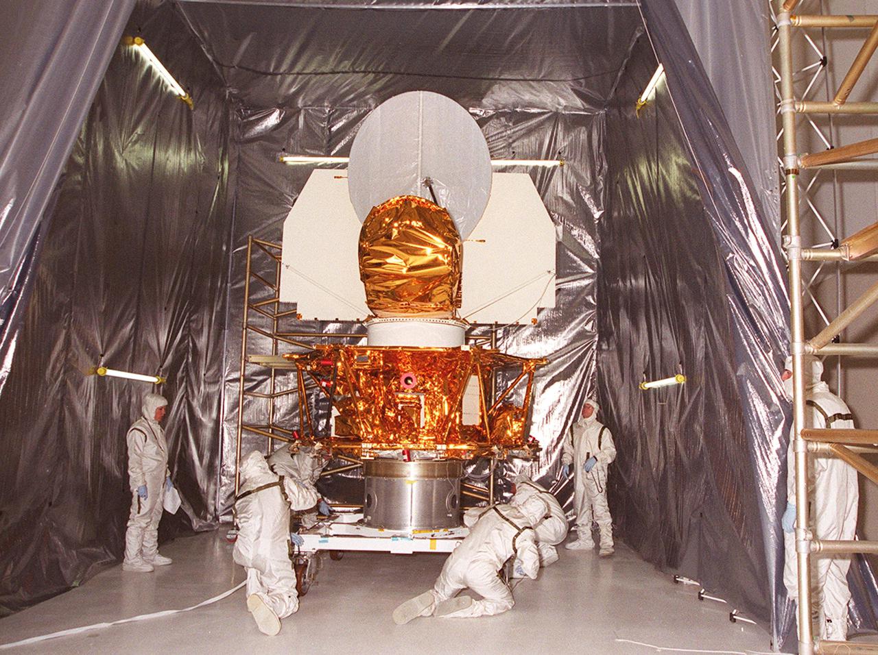 KENNEDY SPACE CENTER, FLA. --  Workers in the Spacecraft Assembly and Encapsulation Facility 2 secure the Microwave Anisotropy Probe (MAP) on a workstand inside a tent. Several milestones must be completed while MAP is at SAEF-2, including antenna installations, solar array installation, solar array deployment and illumination testing, a spacecraft comprehensive performance test, fueling with hydrazine propellant and a spin balance test. MAP will then be ready for integration with the solid propellant Payload Assist Module upper stage booster. MAP is scheduled for launch June 30 from Cape Canaveral Air Force Station on a Delta II rocket into a lunar-assisted trajectory to the Sun-Earth for a 27-month mission. The MAP instrument consists of a set of passively cooled microwave radiometers with 1.4x 1.6-meter diameter primary reflectors to provide the desired angular resolution. MAP measures small fluctuations in the temperature of the cosmic microwave background radiation to an accuracy of one millionth of a degree These measurements should reveal the size, matter content, age, geometry and fate of the universe. They will also reveal the primordial structure that grew to form galaxies and will test ideas about the origins of these primordial structures. The MAP instrument will be continuously shaded from the Sun, Earth, and Moon by the spacecraft. It is a product of Goddard Space Flight Center in partnership with Princeton University