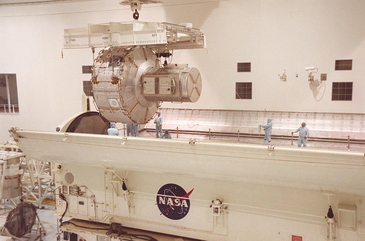 KENNEDY SPACE CENTER, FLA. -- In the Space Station Processing Facility, workers standing inside the payload canister help guide the Joint Airlock Module into place. The airlock will be installed in the payload bay of Atlantis for mission STS-104 to the International Space Station. The airlock is a pressurized flight element consisting of two cylindrical chambers attached end-to-end by a connecting bulkhead and hatch. Once installed and activated, the Airlock becomes the primary path for spacewalk entry to and departure from the Space Station for U.S. spacesuits, which are known as Extravehicular Mobility Units, or EMUs. In addition, the Joint Airlock is designed to support the Russian Orlan spacesuit for EVA activity. STS-104 is scheduled for launch June 14 from Launch Pad 39B