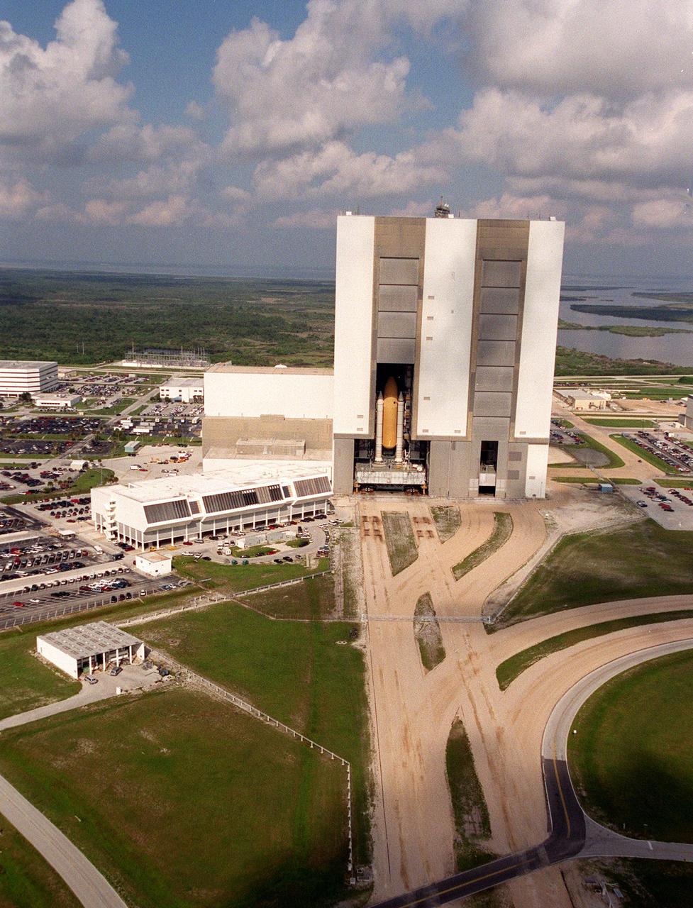 KENNEDY SPACE CENTER, Fla. -- Scattered clouds cast shadows as Space Shuttle Atlantis crawls back inside the Vehicle Assembly Building high bay 1. After earlier starting its trek to Launch Pad 39B, Atlantis was returned to the VAB due to lightning in the area. To the left of the VAB is the Launch Control Center. The four-story building houses the firing rooms that are used to conduct Space Shuttle launches. Leading away from the VAB, in the foreground, is the crawlerway, the 130-foot-wide road specially constructed to transport the Shuttle, mobile launcher platform and crawler-transporter with a combined weight of about 17 million pounds. Space Shuttle Atlantis is targeted for launch no earlier than July 12 on mission STS-104, the 10th flight to the International Space Station. The payload on the 11-day mission is the Joint Airlock Module, which will allow astronauts and cosmonauts in residence on the Station to perform future spacewalks without the presence of a Space Shuttle. The module, which comprises a crew lock and an equipment lock, will be connected to the starboard (right) side of Node 1 Unity. Atlantis will also carry oxygen and nitrogen storage tanks, vital to operation of the Joint Airlock, on a Spacelab Logistics Double Pallet in the payload bay. The tanks, to be installed on the perimeter of the Joint Module during the mission’s spacewalks, will support future spacewalk operations and experiments plus augment the resupply system for the Station’s Service Module