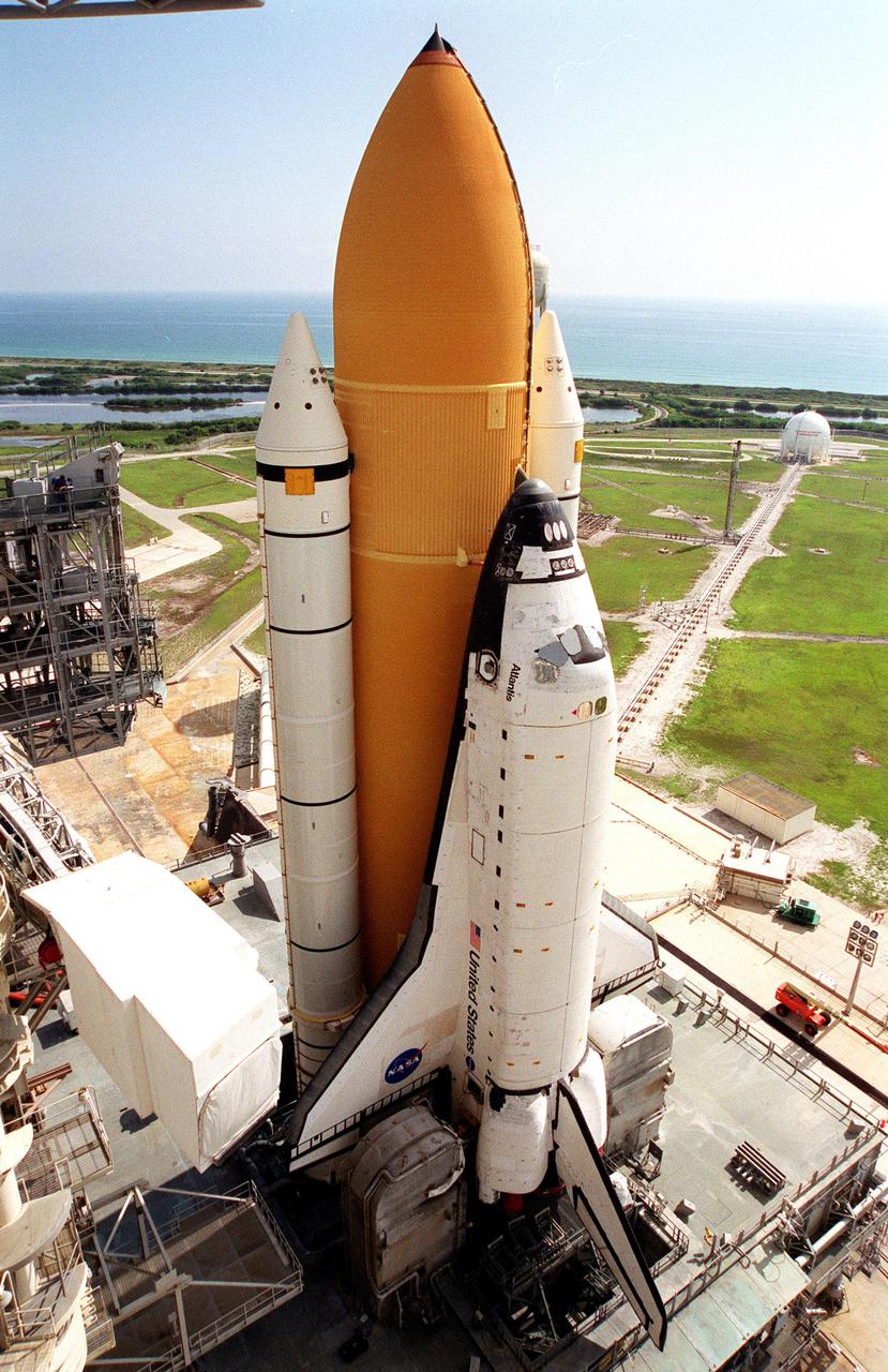 KENNEDY SPACE CENTER, Fla. -- Atop the mobile launcher platform, Space Shuttle Atlantis sits on Launch Pad 39B after rollout from the Vehicle Assembly Building. Seen on either side of the orbiter’s tail are the tail service masts. They support the fluid, gas and electrical requirements of the orbiter’s liquid oxygen and liquid hydrogen aft umbilicals. To the left of the orbiter is the white environmental chamber (white room) that mates with the orbiter and holds six persons. It provides access to the orbiter crew compartment. In the background is the Atlantic Ocean. The Shuttle is targeted for launch no earlier than July 12 on mission STS-104, the 10th flight to the International Space Station. The payload on the 11-day mission is the Joint Airlock Module, which will allow astronauts and cosmonauts in residence on the Station to perform future spacewalks without the presence of a Space Shuttle. The module, which comprises a crew lock and an equipment lock, will be connected to the starboard (right) side of Node 1 Unity. Atlantis will also carry oxygen and nitrogen storage tanks, vital to operation of the Joint Airlock, on a Spacelab Logistics Double Pallet in the payload bay. The tanks, to be installed on the perimeter of the Joint Module during the mission’s spacewalks, will support future spacewalk operations and experiments plus augment the resupply system for the Station’s Service Module