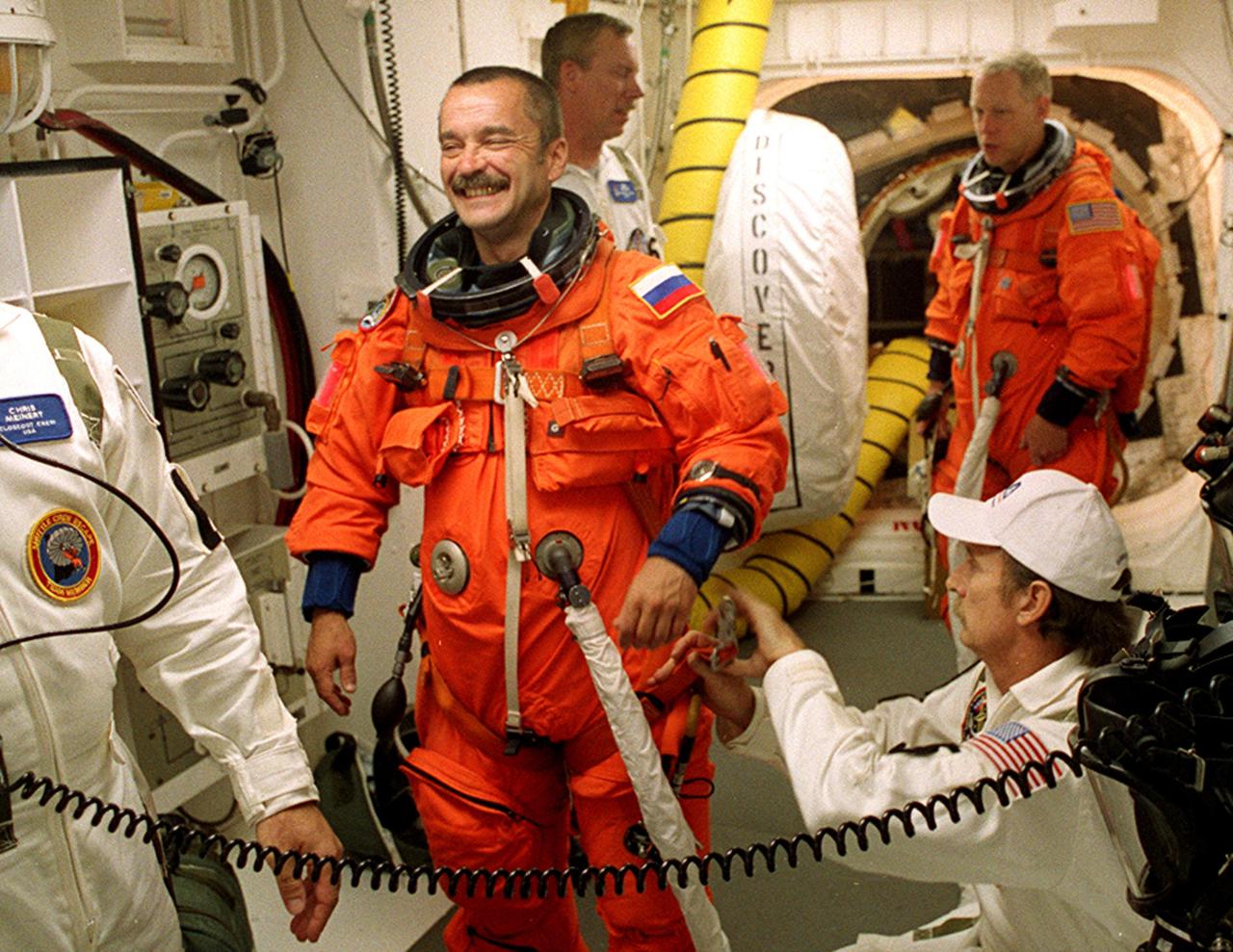 KENNEDY SPACE CENTER, Fla. - In the White Room, Launch Pad 39A, Expedition Three crew member Mikhail Tyurin is assisted with his flight equipment before entering Space Shuttle Discovery for launch. With him are (left) Orbiter Vehicle Closeout Chief Chris Meinert and USA Mechanical Technician Al Schmidt. In the background is STS-105 Mission Specialist Patrick Forrester. The payload on the STS-105 mission to the International Space Station the third flight of the Italian-built Multi-Purpose Logistics Module Leonardo, delivering additional scientific racks, equipment and supplies for the Space Station, and the Early Ammonia Servicer (EAS) tank. The EAS, which will be attached to the Station during two spacewalks, contains spare ammonia for the Station’s cooling system. Also, the Expedition Three crew is aboard to replace the Expedition Two crew on the International Space Station, who will be returning to Earth aboard Discovery after a five-month stay on the Station