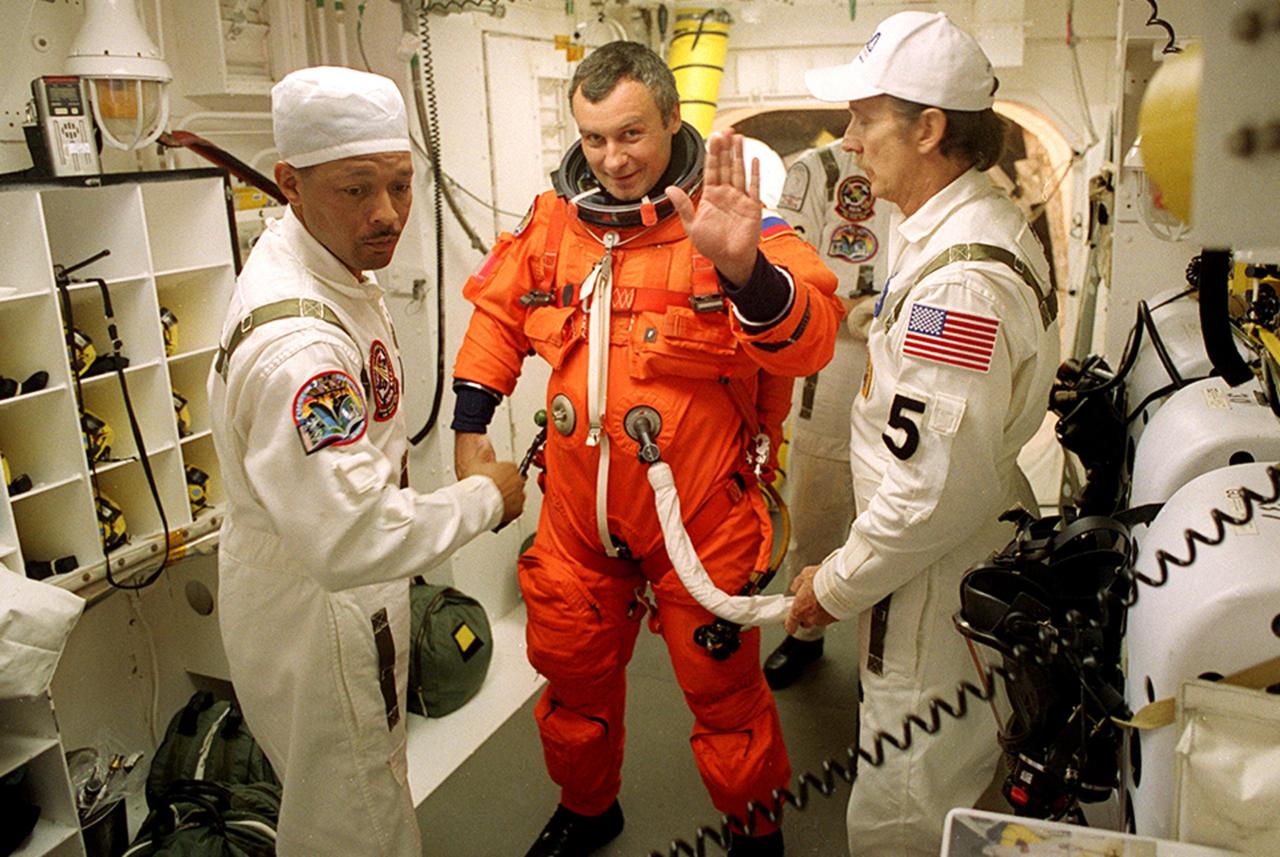 KENNEDY SPACE CENTER, Fla. - Expedition Three crew member Vladimir Dezhurov waves as he is helped with his launch and entry suit before he enters Space Shuttle Discovery for launch. Helping him are (left) NASA Astronaut Support Personnel John Herrington and (right) USA Mechanical Technician Al Schmidt. The payload on the STS-105 mission to the International Space Station includes the third flight of the Italian-built Multi-Purpose Logistics Module Leonardo, delivering additional scientific racks, equipment and supplies for the Space Station, and the Early Ammonia Servicer (EAS) tank. The EAS, which will be attached to the Station during two spacewalks, contains spare ammonia for the Station’s cooling system. Also, the Expedition Three crew is aboard to replace the Expedition Two crew on the International Space Station, who will be returning to Earth aboard Discovery after a five-month stay on the Station