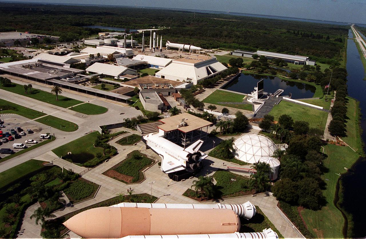 KENNEDY SPACE CENTER, Fla. --  This aerial view of the KSC Visitor Complex shows many of the buildings and exhibits, such as the full-scale solid rocket boosters and external tank in the foreground, a full-scale model of a Space Shuttle orbiter behind them, the Launch Status Dome to the right, and the Astronauts Memorial Space Mirror next to the retention pond.  Names of the 17 American astronauts who gave their lives to the quest to explore space are engraved in the mirror-finished surface of this memorial exhibit.  Sunlight projecting through the names appears to emblazon them against a reflection of the sky.  To the left of the mirror is the Center for Space Education.  In the background is the Rocket Garden, exhibiting early rockets from the space program