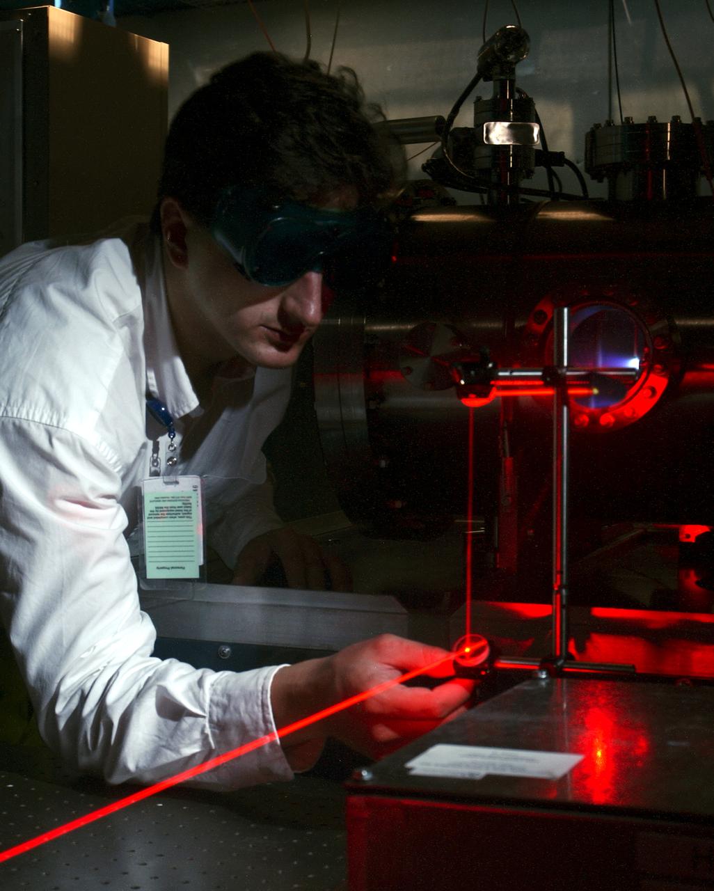Dr. Tom Markusic, a propulsion research engineer at the Marshall Space Flight Center (MSFC), adjusts a diagnostic laser while a pulsed plasma thruster (PPT) fires in a vacuum chamber in the background. NASA/MSFC's Propulsion Research Center (PRC) is presently investigating plasma propulsion for potential use on future nuclear-powered spacecraft missions, such as human exploration of Mars.
