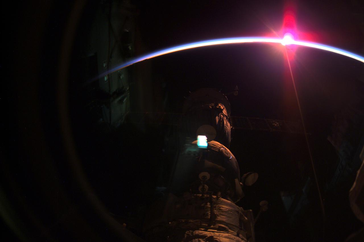 The setting sun and the thin blue airglow line at Earth's horizon was captured by the International Space Station's (ISS) Expedition Three crewmembers with a digital camera. Some of the Station's components are silhouetted in the foreground. The crew was launched aboard the Space Shuttle Orbiter Discovery STS-105 mission, on August 10, 2001, replacing the Expedition Two crew. After marning the orbiting ISS for 128 consecutive days, the three returned to Earth on December 17, 2001, aboard the STS-108 mission Space Shuttle Orbiter Endeavour.
