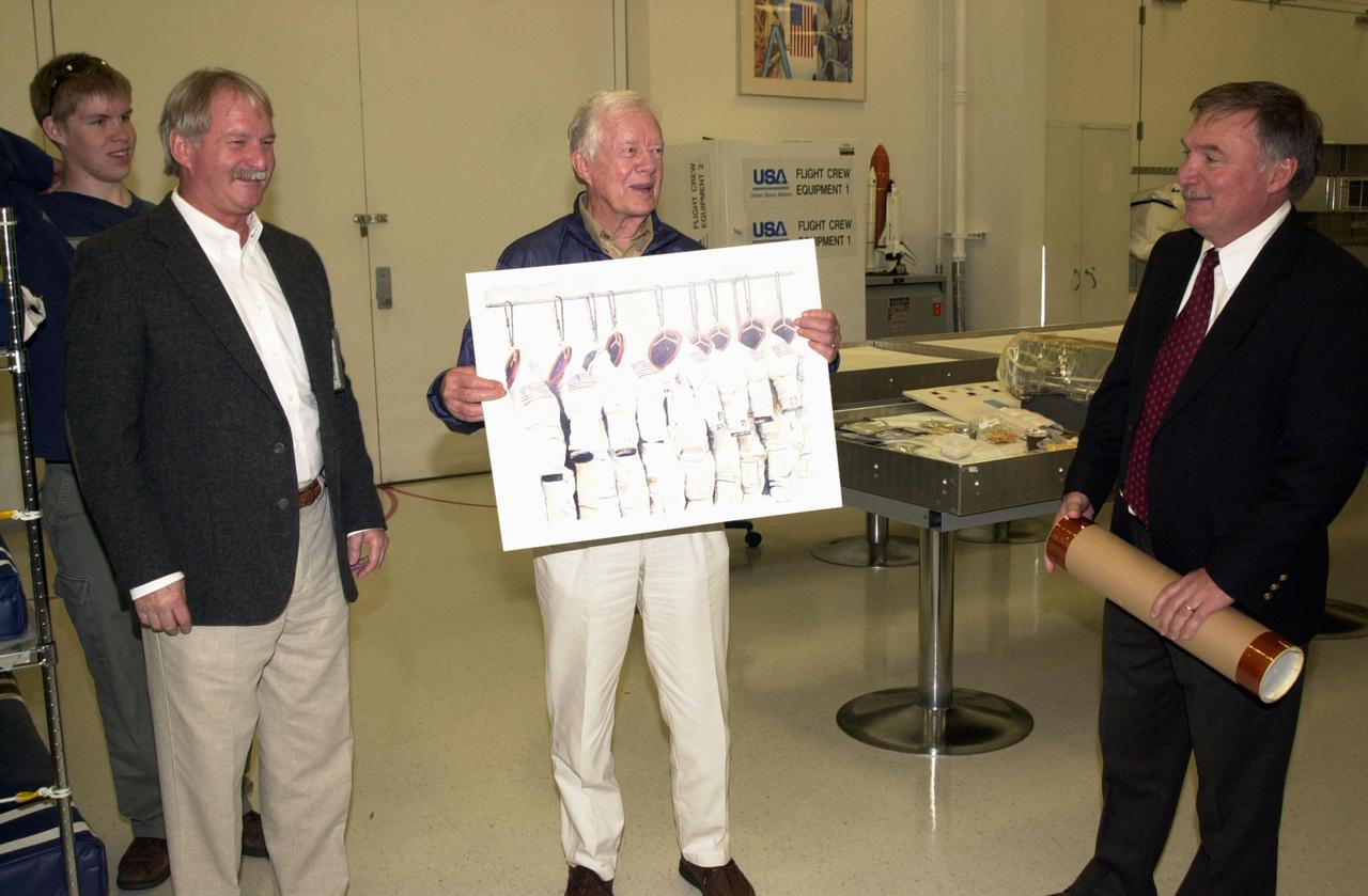 KENNEDY SPACE CENTER, FLA. -- During a tour of KSC, former President Jimmy Carter is presented with a print displaying the space suits used in the early days of the Space Program. is Tip Talone (right), director of Payload Processing, International Space Station, made the presentation.  At left is Ron Woods, a technician in the Flight Crew Equipment Facility, who is also the artist of the original drawing