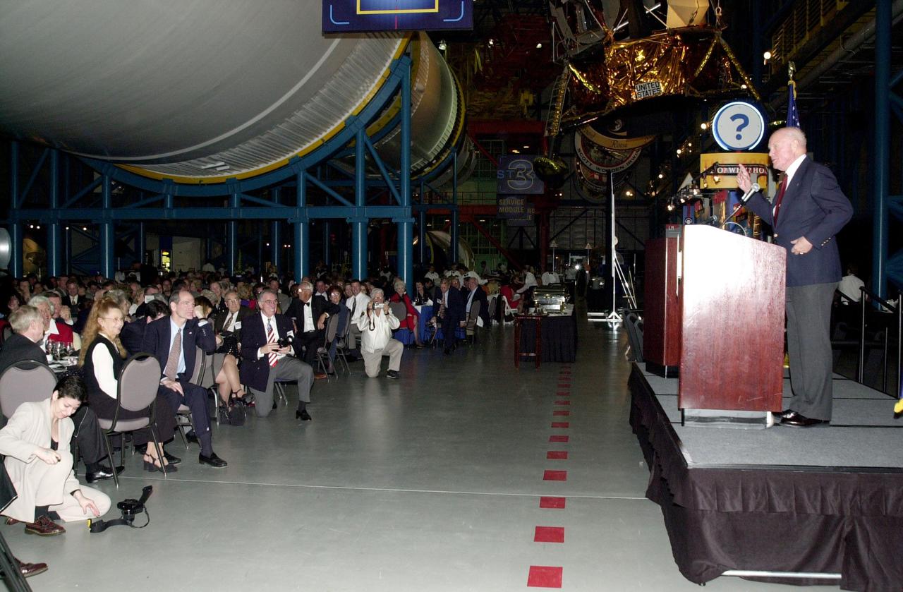 KENNEDY SPACE CENTER, FLA. - In the Apollo_Saturn V Center at KSC, guests enjoy the comments of John Glenn Jr. during the dinner celebration of the 40th anniversary of American spaceflight.  In the background is the Saturn V rocket.  Glenn was the first American to orbit the Earth, aboard the Friendship 7 spacecraft.   That journey lasted nearly five hours.  In 1998, 36 years later, Glenn flew on Space Shuttle Discovery on mission STS-95, orbiting the Earth for 218 hours