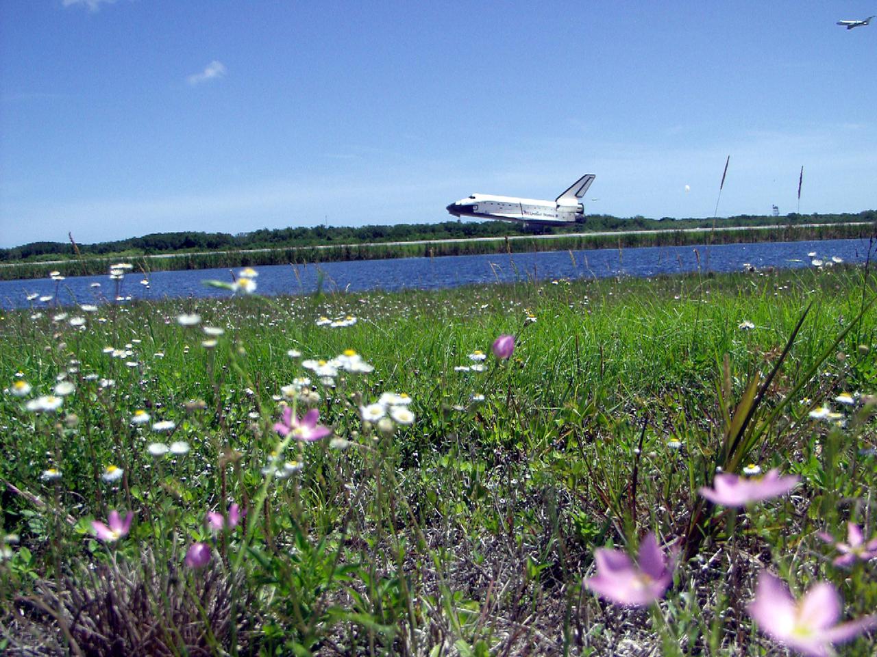 KENNEDY SPACE CENTER, FLA. - A field of wild flowers greets Atlantis as it touches down on runway 33 at KSC, the drag chute just deployed. The landing completes the 10-day, 19-hour, 4.5-million mile mission STS-110 to the International Space Station. In the upper right corner is the chase plane following Atlantis' path. The orbiter carries the returning crew Commander Michael Bloomfield, Pilot Stephen Frick and Mission Specialists Jerry Ross, Steven Smith, Ellen Ochoa, Lee Morin and Rex Walheim. Main gear touchdown was 12:26:57 p.m. EDT, nose gear touchdown was 12:27:09 p.m. and wheel stop was 12:28:07 p.m. The crew delivered and installed the S0 truss, which will support cooling and power systems essential for the addition of future international laboratories, on the Station.