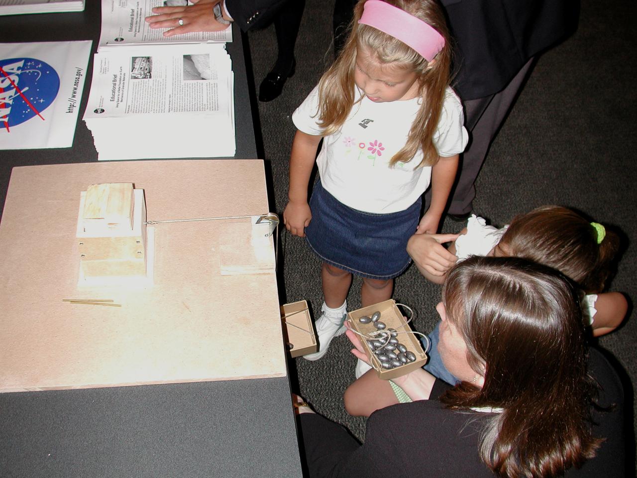 Twila Schneider of Infinity Technology in Huntsville, AL, uses a small sand displacement box to explain the principles of the Mechanics of Granular Materials (MGM-III) experiment to two young Virginia students. The activity was part of the Space Research and You education event held by NASA's Office of Biological and Physical Research on June 25, 2002, in Arlington, VA, to highlight the research that will be conducted on STS-107.