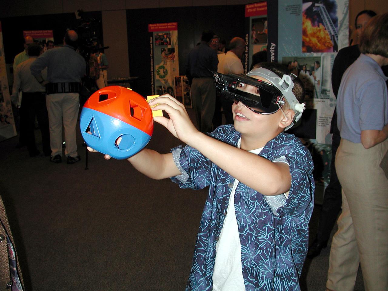 A student tries to insert plastic blocks into the correct holes in a baby's toy. The seemingly trivial task becomes nearly impossible when the prism glasses he is wearing reverse left and right. This is similar to tests used to measure how astronauts adapt to space and then readapt to Earth. The activity was part of the Space Research and You education event held by NASA's Office of Biological and Physical Research on June 25, 2002, in Arlington, VA, to highlight the research that will be conducted on STS-107.