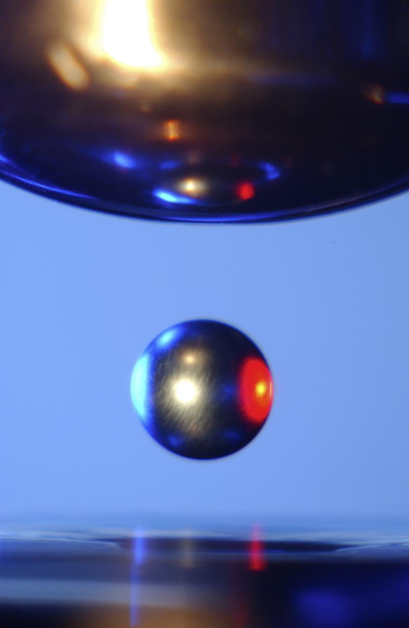 This is a close-up of a sample of titanium-zirconium-nickel alloy inside the Electrostatic Levitator (ESL) vacuum chamber at NASA's Marshall Space Flight Center (MSFC). The ESL uses static electricity to suspend an object (about 3-4 mm in diameter) inside a vacuum chamber allowing scientists to record a wide range of physical properties without the sample contracting the container or any instruments, conditions that would alter the readings. Once inside the chamber, a laser heats the sample until it melts. The laser is then turned off and the sample cools, changing from a liquid drop to a solid sphere. Since 1977, the ESL has been used at MSFC to study the characteristics of new metals, ceramics, and glass compounds. Materials created as a result of these tests include new optical materials, special metallic glasses, and spacecraft components.