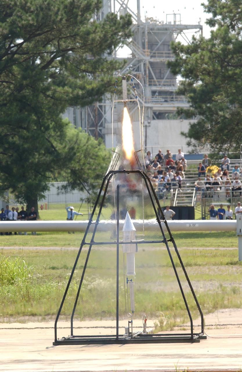 In honor of the Centernial of Flight Celebration and commissioned by the American Institute of Aeronautics and Astronautics (AIAA), a team of engineers from Marshall Space Flight Center (MSFC) built a replica of the first liquid-fueled rocket. The original rocket, designed and built by rocket engineering pioneer Robert H. Goddard in 1926, opened the door to modern rocketry. Goddard's rocket reached an altitude of 41 feet while its flight lasted only 2.5 seconds. The Marshall design team's plan was to stay as close as possible to an authentic reconstruction of Goddard's rocket. The same propellants were used - liquid oxygen and gasoline - as available during Goddard's initial testing and firing. The team also tried to construct the replica using the original materials and design to the greatest extent possible. By purposely using less advanced techniques and materials than many that are available today, the team encountered numerous technical challenges in testing the functional hardware. There were no original blueprints or drawings, only photographs and notes. However, this faithful adherence to historical accuracy has allowed the team to experience many of the same challenges Goddard faced 77 years ago, and more fully appreciate the genius of this extraordinary man. In this photo, the replica is shown firing in the A-frame launch stand in near-flight configuration at MSFC's Test Area 116 during the American Institute of Aeronautics and Astronautics 39th Joint Propulsion Conference on July 23, 2003.