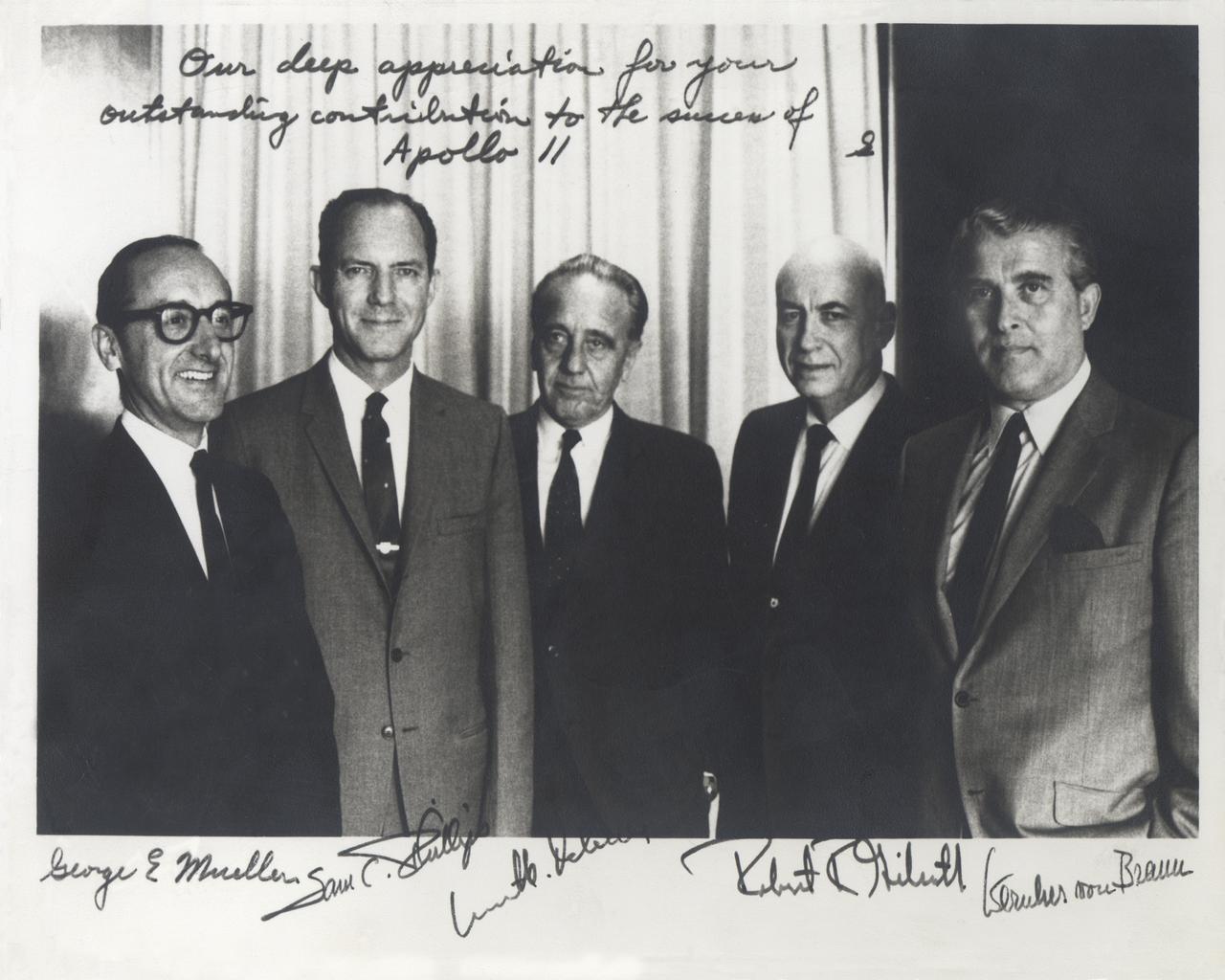 This historical photograph is of the Apollo Space Program Leaders.  An inscription appears at the top of the image that states, “Our deep appreciation for your outstanding contribution to the success of Apollo 11”, signed “S”, indicating that it was originally signed by Apollo Program Director General Sam Phillips, pictured second from left. From left to right are; NASA Associate Administrator George Mueller; Phillips; Kurt Debus, Director of the Kennedy Space Center; Robert Gilruth, Director of the Manned Spacecraft Center, later renamed the Johnson Space Center; and Wernher von Braun, Director of the Marshall Space Flight Center.