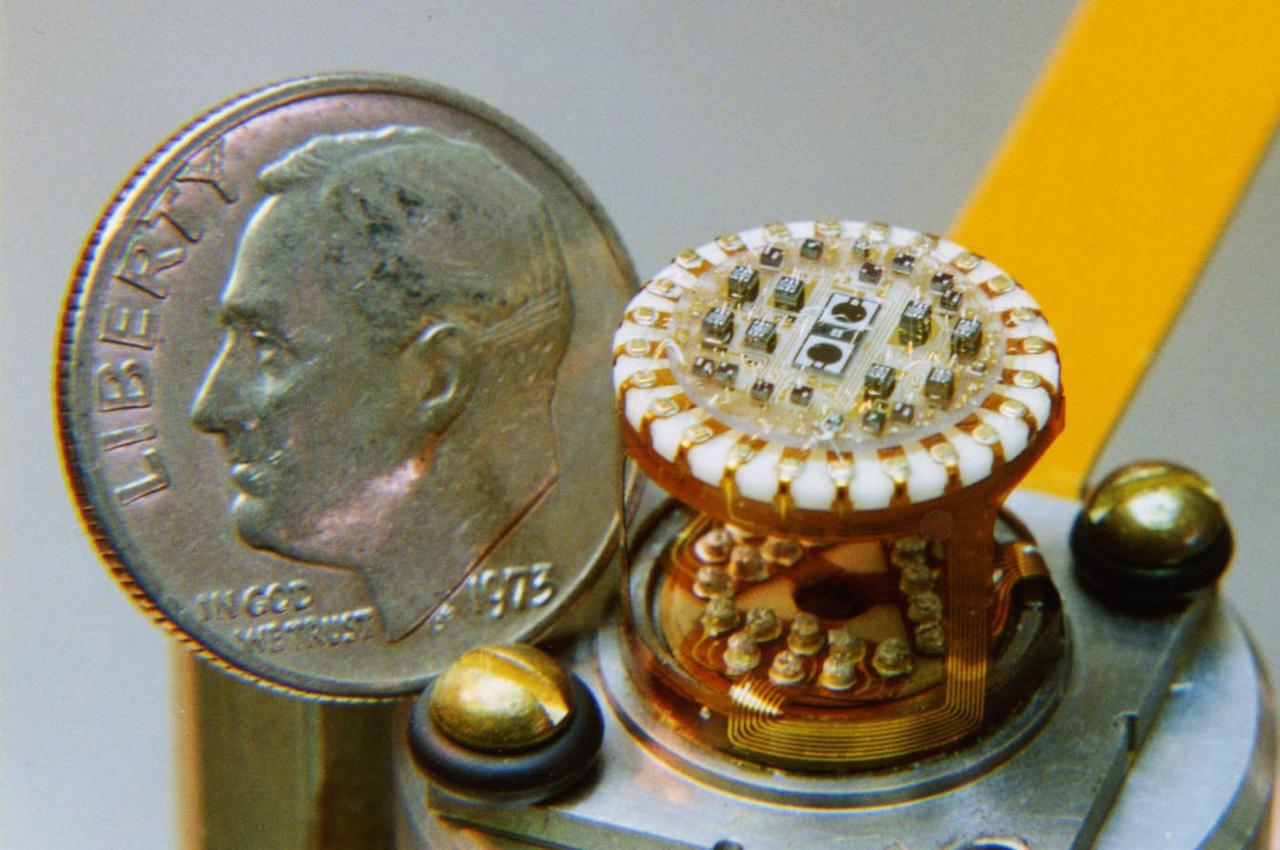 In this photo, the Gravity Probe B (GP-B) detector mount assembly is shown in comparison to the size of a dime.  The assembly is used to detect exactly how much starlight is coming through different beams from the beam splitter in the telescope.  The measurements from the tiny chips inside are what keeps GP-B aimed at the guide star. The GP-B is the relativity experiment developed at Stanford University to test two extraordinary predictions of Albert Einstein’s general theory of relativity. The experiment will measure, very precisely, the expected tiny changes in the direction of the spin axes of four gyroscopes contained in an Earth-orbiting satellite at a 400-mile altitude. So free are the gyroscopes from disturbance that they will provide an almost perfect space-time reference system. They will measure how space and time are very slightly warped by the presence of the Earth, and, more profoundly, how the Earth’s rotation very slightly drags space-time around with it. These effects, though small for the Earth, have far-reaching implications for the nature of matter and the structure of the Universe. GP-B is among the most thoroughly researched programs ever undertaken by NASA. This is the story of a scientific quest in which physicists and engineers have collaborated closely over many years. Inspired by their quest, they have invented a whole range of technologies that are already enlivening other branches of science and engineering.  Launched  April 20, 2004 , the GP-B program was managed for NASA by the Marshall Space Flight Center. Development of the GP-B is the responsibility of Stanford University along with major subcontractor Lockheed Martin Corporation.  (Image credit to Paul Ehrensberger, Stanford University.)