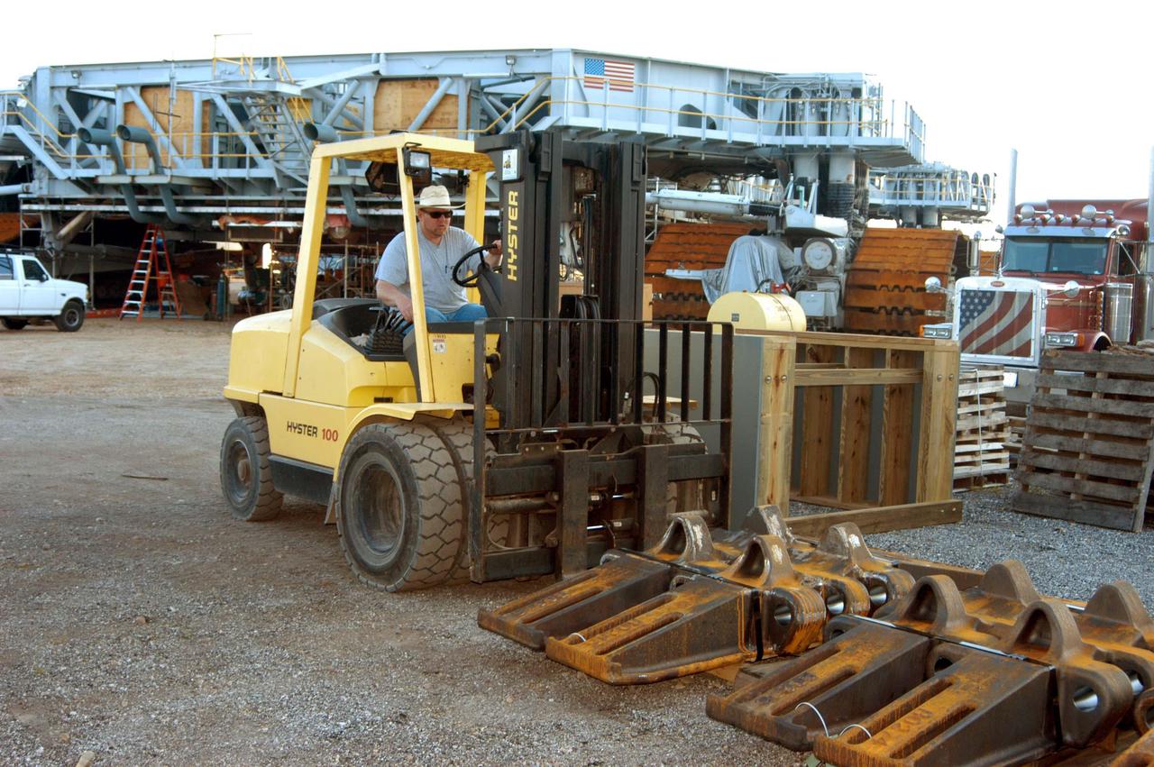 KENNEDY SPACE CENTER, FLA. - In the Crawler Transporter (CT) area, a worker offloads some of the new crawler shoes that arrived from Minnesota. In the background is one of the two CTs. The new shoes were manufactured by ME Global in Duluth, Minn. The CT transports the Mobile Launcher Platform, with the assembled Space Shuttle aboard, between the refurbishment area, the VAB and Launch Complex Pads 39A and 39B. The crawlers have 456 shoes, 57 per belt (8 belts in all). Each shoe weighs 2,200 pounds. The original shoes were manufactured for the Apollo Program. Cracks appeared in the shoes in recent years spurring a need for replacement. The new manufacturer, in Duluth, Minn., has improved the design for Return to Flight and use through the balance of the Space Shuttle Program.