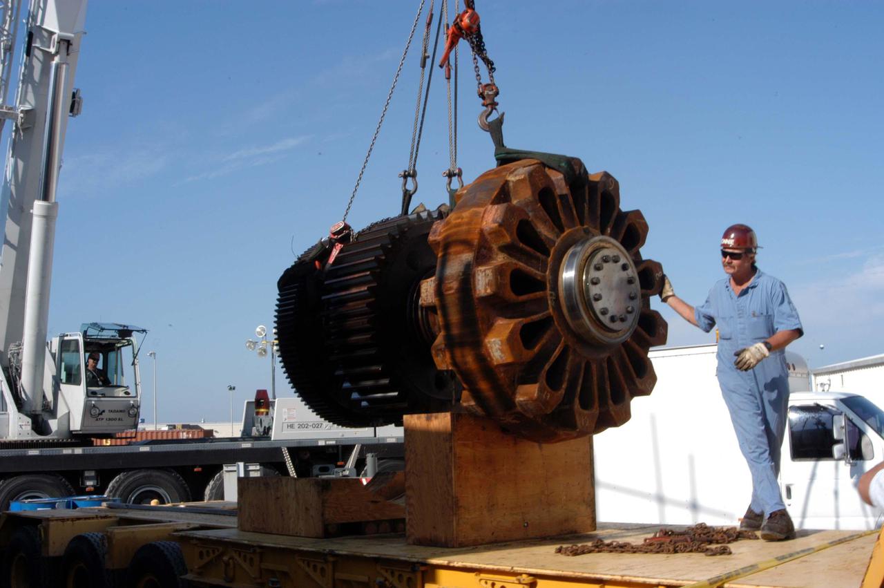 KENNEDY SPACE CENTER, FLA. -   A worker watches as the giant-sized gear (left side) and sprocket (right side) is moved.  It will be installed on a Crawler-Tranporter (CT).  The drive sprocket turns the belt on the CT.  The sprocket is mated to the gear that attaches to the drive motor.  The CT travels on eight tracked tread belts, each containing 57 tread belt shoes, for a combined weight of 957,600 pounds.  The CT carries the Space Shuttle atop its Mobile Launcher Platform, adding another 12 million pounds, from the Vehicle Assembly Building to the launch pad.  NASA and United Space Alliance (USA) CT system engineers and USA technicians are repairing the sprockets and rollers on each belt before new shoes are installed.  Replacement of the sprockets, gears and shoes is part of the most extensive maintenance work performed on the CT in its history.