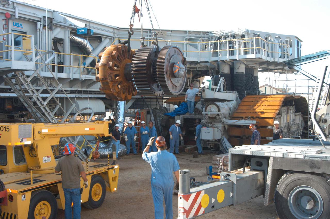 KENNEDY SPACE CENTER, FLA. -   The giant-sized sprocket (left) and gear (right) is moved toward the Crawler-Transporter in the background for installation. The drive sprocket turns the belt on the CT.  The sprocket is mated to the gear that attaches to the drive motor.  The CT travels on eight tracked tread belts, each containing 57 tread belt shoes, for a combined weight of 957,600 pounds.  The CT carries the Space Shuttle atop its Mobile Launcher Platform, adding another 12 million pounds, from the Vehicle Assembly Building to the launch pad.  NASA and United Space Alliance (USA) CT system engineers and USA technicians are repairing the sprockets and rollers on each belt before new shoes are installed.  Replacement of the sprockets, gears and shoes is part of the most extensive maintenance work performed on the CT in its history.