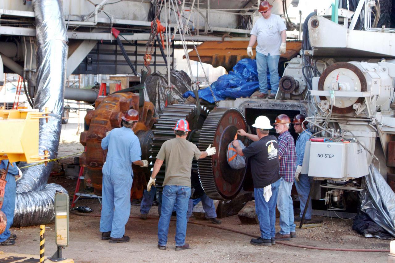 KENNEDY SPACE CENTER, FLA. -   Workers maneuver the giant-sized sprocket (left side) and gear (right side) for installation on the Crawler-Transporter behind it.  The drive sprocket turns the belt on the CT.  The sprocket is mated to the gear that attaches to the drive motor.  The CT travels on eight tracked tread belts, each containing 57 tread belt shoes, for a combined weight of 957,600 pounds.  The CT carries the Space Shuttle atop its Mobile Launcher Platform, adding another 12 million pounds, from the Vehicle Assembly Building to the launch pad.  NASA and United Space Alliance (USA) CT system engineers and USA technicians are repairing the sprockets and rollers on each belt before new shoes are installed.  Replacement of the sprockets, gears and shoes is part of the most extensive maintenance work performed on the CT in its history.