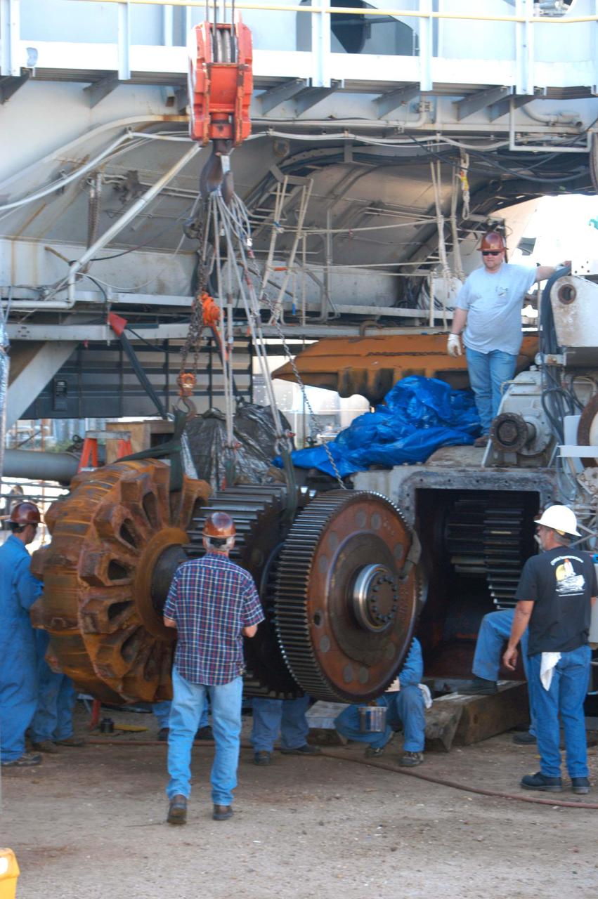 KENNEDY SPACE CENTER, FLA. -   Workers get ready to install the giant-sized sprocket (left side) and gear (right side) on the Crawler-Transporter behind it.The drive sprocket turns the belt on the CT.  The sprocket is mated to the gear that attaches to the drive motor.  The CT travels on eight tracked tread belts, each containing 57 tread belt shoes, for a combined weight of 957,600 pounds.  The CT carries the Space Shuttle atop its Mobile Launcher Platform, adding another 12 million pounds, from the Vehicle Assembly Building to the launch pad.  NASA and United Space Alliance (USA) CT system engineers and USA technicians are repairing the sprockets and rollers on each belt before new shoes are installed.  Replacement of the sprockets, gears and shoes is part of the most extensive maintenance work performed on the CT in its history.