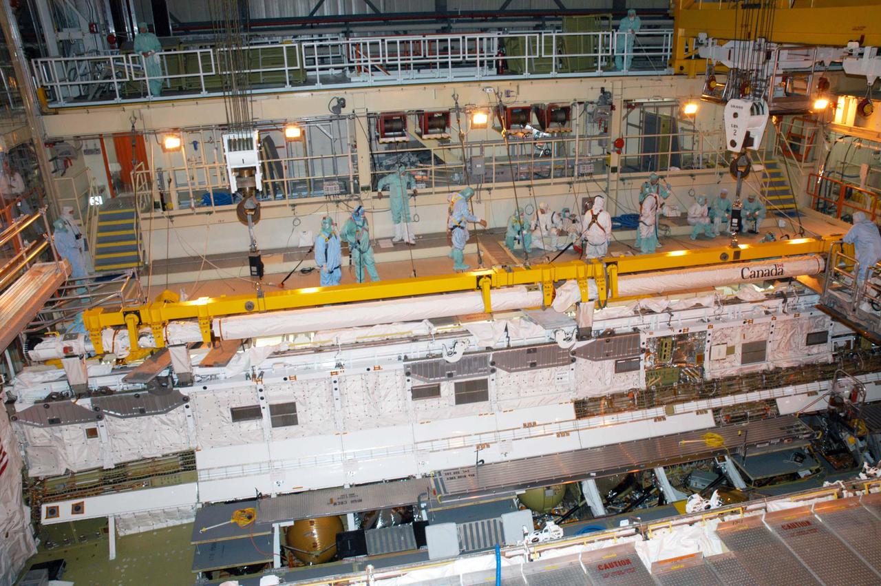 KENNEDY SPACE CENTER, FLA. - Technicians in the Orbiter Processing Facility work to install the Remote Manipulator System (RMS), also known as the Canadian robotic arm, in Discovery’s payload bay.  The RMS is used to deploy and retrieve payloads, provide a mobile extension ladder or foot restraints for crew members during extravehicular activities; and to aid the flight crew members in viewing surfaces of the orbiter or payloads through a television camera on the RMS. The arm is also serving as the base for the new Orbiter Boom Sensor System (OBSS), one of the safety measures for Return to Flight, equipping the Shuttle with cameras and laser systems to inspect the Shuttle’s Thermal Protection System while in space.  Discovery is scheduled for a launch planning window of May 2005 on Return to Flight mission STS-114.