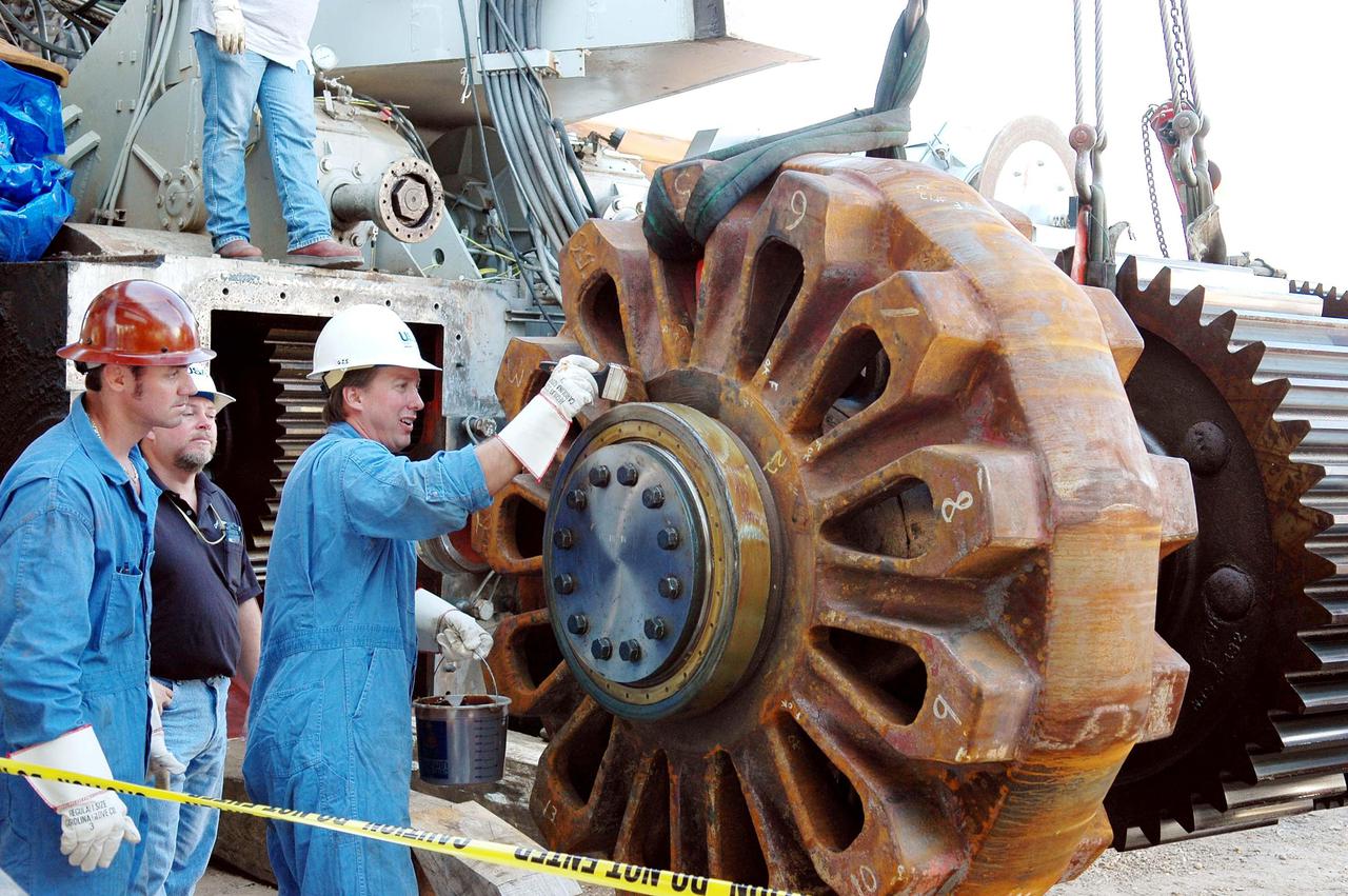 KENNEDY SPACE CENTER, FLA. -   A worker greases the giant sprocket that will be installed on the Crawler-Transporter (background).  The drive sprocket turns the belt on the CT.  The sprocket is mated to the gear that attaches to the drive motor.  The CT travels on eight tracked tread belts, each containing 57 tread belt shoes, for a combined weight of 957,600 pounds.  The CT carries the Space Shuttle atop its Mobile Launcher Platform, adding another 12 million pounds, from the Vehicle Assembly Building to the launch pad.  NASA and United Space Alliance (USA) CT system engineers and USA technicians are repairing the sprockets and rollers on each belt before new shoes are installed.  Replacement of the sprockets, gears and shoes is part of the most extensive maintenance work performed on the CT in its history.