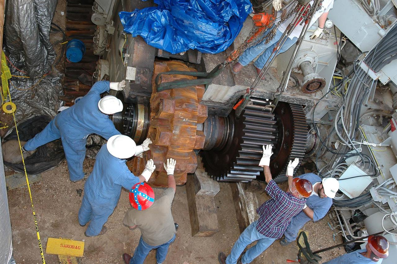 KENNEDY SPACE CENTER, FLA. -   Workers maneuver the giant sprocket (left) and attached gear (right) into position on the Crawler-Transporter.  The drive sprocket turns the belt on the CT.  The sprocket is mated to the gear that attaches to the drive motor.  The CT travels on eight tracked tread belts, each containing 57 tread belt shoes, for a combined weight of 957,600 pounds.  The CT carries the Space Shuttle atop its Mobile Launcher Platform, adding another 12 million pounds, from the Vehicle Assembly Building to the launch pad.  NASA and United Space Alliance (USA) CT system engineers and USA technicians are repairing the sprockets and rollers on each belt before new shoes are installed.  Replacement of the sprockets, gears and shoes is part of the most extensive maintenance work performed on the CT in its history.