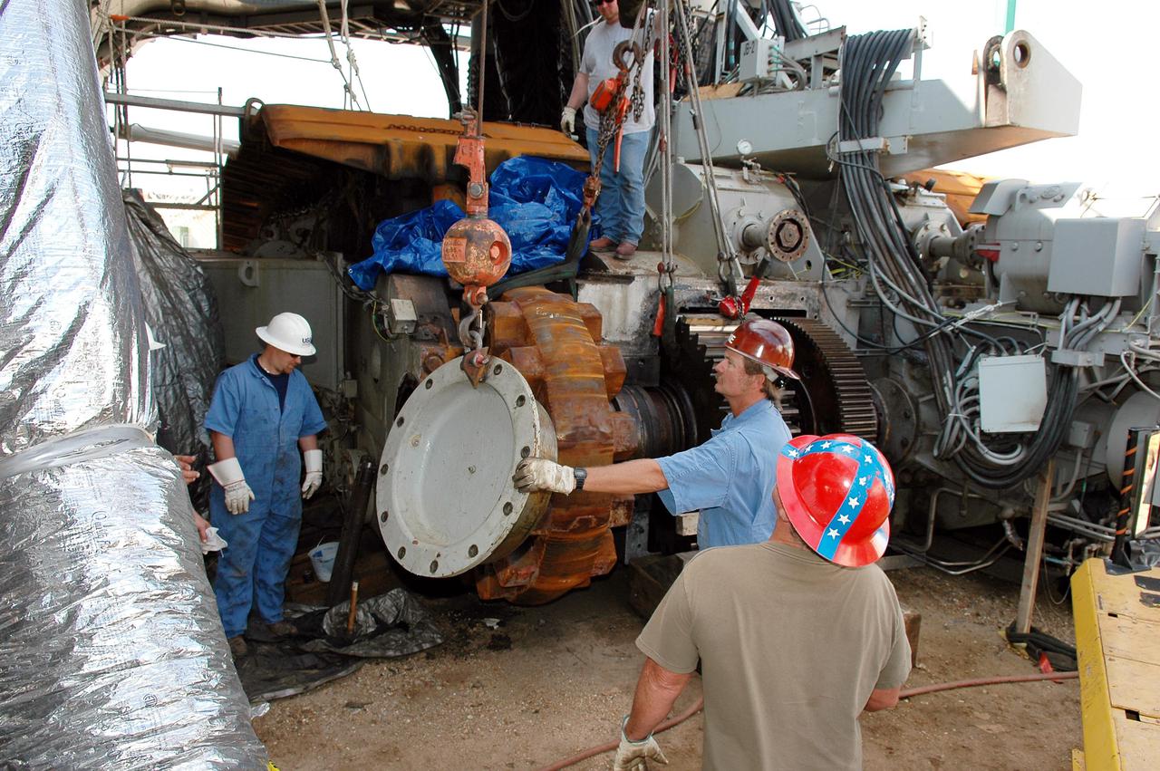 KENNEDY SPACE CENTER, FLA. -   Workers move the hub toward the gear, where it will be attached, on the Crawler-Transporter.   The drive sprocket turns the belt on the CT.  The sprocket is mated to the gear that attaches to the drive motor.  The CT travels on eight tracked tread belts, each containing 57 tread belt shoes, for a combined weight of 957,600 pounds.  The CT carries the Space Shuttle atop its Mobile Launcher Platform, adding another 12 million pounds, from the Vehicle Assembly Building to the launch pad.  NASA and United Space Alliance (USA) CT system engineers and USA technicians are repairing the sprockets and rollers on each belt before new shoes are installed.  Replacement of the sprockets, gears and shoes is part of the most extensive maintenance work performed on the CT in its history.