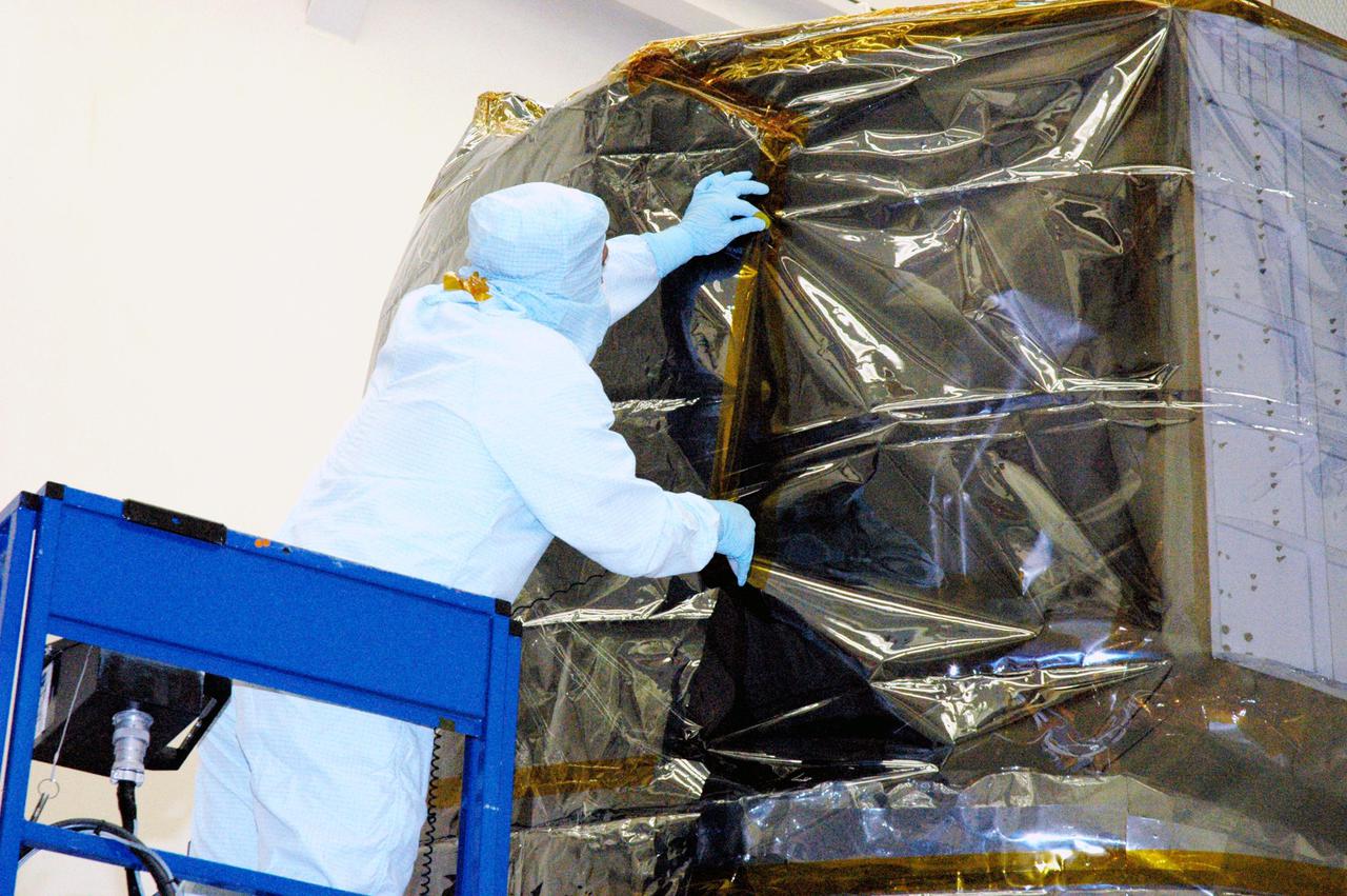 KENNEDY SPACE CENTER, FLA. - In Hangar AE at Cape Canaveral Air Force Station (CCAFS) in Florida, technicians with Spectrum Astro Inc. secure the plastic cover around the Swift spacecraft before moving it to the launch pad. The launch of the Swift observatory, a NASA spacecraft to pinpoint the location of gamma-ray bursts, is scheduled for Nov. 17 from Pad 17-A on CCAFS. Liftoff aboard a Boeing Delta II rocket is targeted at the opening of a one-hour launch window beginning at 12:09 p.m. EST. Gamma-ray bursts are distant, yet fleeting explosions that appear to signal the births of black holes. They are the most powerful explosions known in the universe, emitting more than 100 billion times the energy that the Sun emits in a year. Yet they last only from a few milliseconds to a few minutes, never to appear in the same spot again.