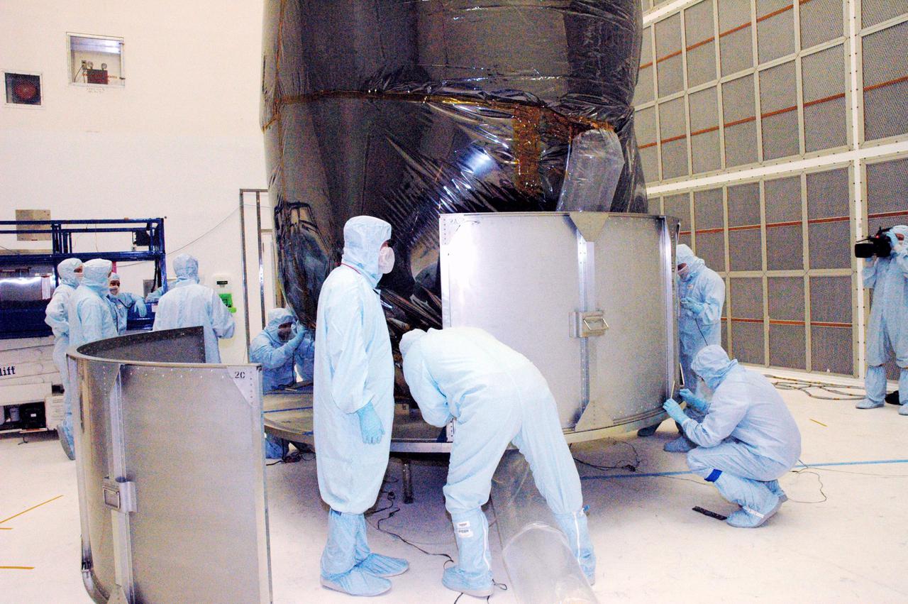 KENNEDY SPACE CENTER, FLA. - Boeing technicians in Hangar AE at Cape Canaveral Air Force Station (CCAFS) in Florida install the lower part of the payload transfer canister around the plastic-wrapped Swift spacecraft. The launch of the Swift observatory, a NASA spacecraft to pinpoint the location of gamma-ray bursts, is scheduled for Nov. 17 from Pad 17-A on CCAFS. Liftoff aboard a Boeing Delta II rocket is targeted at the opening of a one-hour launch window beginning at 12:09 p.m. EST. Gamma-ray bursts are distant, yet fleeting explosions that appear to signal the births of black holes. They are the most powerful explosions known in the universe, emitting more than 100 billion times the energy that the Sun emits in a year. Yet they last only from a few milliseconds to a few minutes, never to appear in the same spot again.