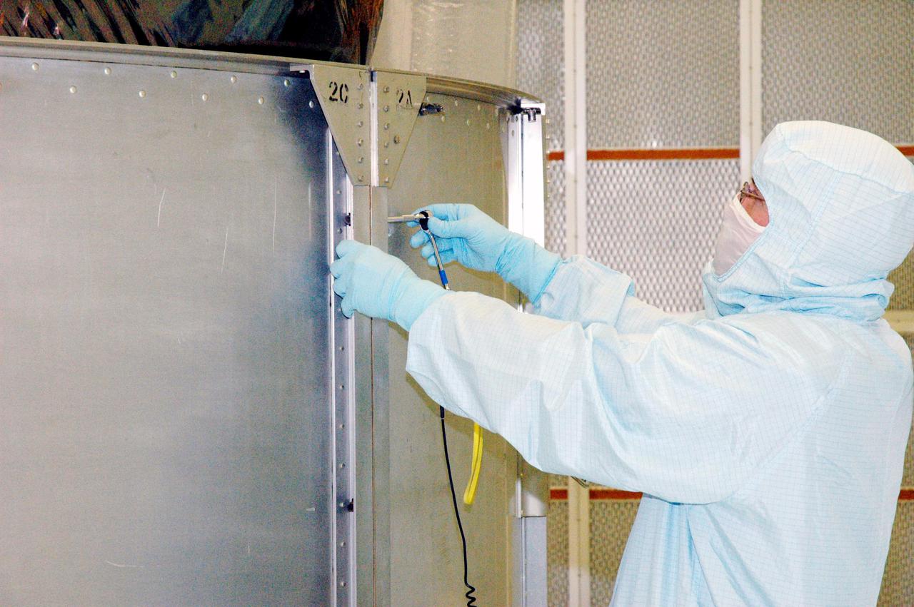KENNEDY SPACE CENTER, FLA. - A Boeing technician in Hangar AE at Cape Canaveral Air Force Station (CCAFS) in Florida attaches two of the lower segments of the payload transfer canister being installed around the plastic-wrapped Swift spacecraft. The launch of the Swift observatory, a NASA spacecraft to pinpoint the location of gamma-ray bursts, is scheduled for Nov. 17 from Pad 17-A on CCAFS. Liftoff aboard a Boeing Delta II rocket is targeted at the opening of a one-hour launch window beginning at 12:09 p.m. EST. Gamma-ray bursts are distant, yet fleeting explosions that appear to signal the births of black holes. They are the most powerful explosions known in the universe, emitting more than 100 billion times the energy that the Sun emits in a year. Yet they last only from a few milliseconds to a few minutes, never to appear in the same spot again.