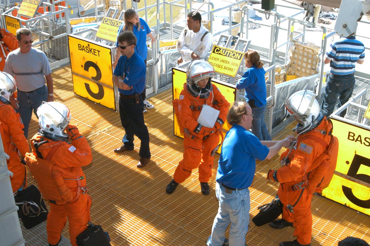 KENNEDY SPACE CENTER, FLA. -  On Launch Pad 39-A, team members (in blue) help astronaut-suited co-workers near the slidewire baskets prepare for an emergency egress scenario. The four-hour exercise simulated normal launch countdown operations, with the added challenge of a fictitious event causing an evacuation of the vehicle and launch pad.  It tested the team’s rescue approaches on the Fixed Service Structure, slidewire basket evacuation, triage care and transportation of injured personnel to hospitals, as well as communications and coordination.
