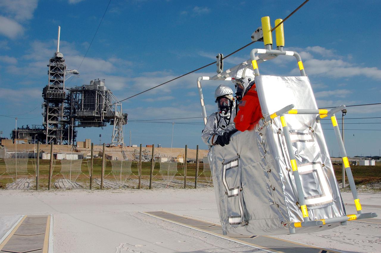 KENNEDY SPACE CENTER, FLA. -  On Launch Pad 39A, a rescue team member and astronaut-suited worker approach landing in a slidewire basket reaching from the Fixed Service Structure in the background during an emergency egress scenario. The four-hour exercise simulated normal launch countdown operations, with the added challenge of a fictitious event causing an evacuation of the vehicle and launch pad.  It tested the team’s rescue approaches on the Fixed Service Structure, slidewire basket evacuation, triage care and transportation of injured personnel to hospitals, as well as communications and coordination.