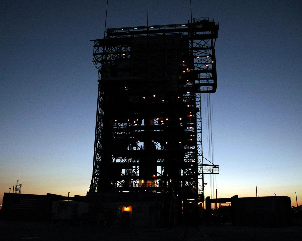 KENNEDY SPACE CENTER, FLA. - In the pre-dawn hours on Launch Pad 17-B at Cape Canaveral Air Force Station, the mobile service tower is silhouetted with the Boeing Delta II rocket that will launch NASA’s Deep Impact spacecraft. The Delta II waits for the arrival and mating of the second stage. A NASA Discovery mission, Deep Impact will probe beneath the surface of Comet Tempel 1 on July 4, 2005, when the comet is 83 million miles from Earth, and reveal the secrets of its interior. After releasing an impactor on a course to hit the comet’s sunlit side, Deep Impact’s flyby spacecraft will collect pictures and data of how the crater forms, measure the crater’s depth and diameter, as well as the composition of the interior of the crater and any material thrown out, and determine the changes in natural outgassing produced by the impact. It will send the data back to Earth through the antennas of the Deep Space Network.