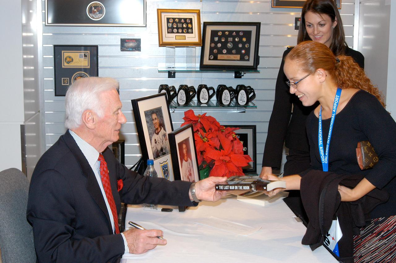 KENNEDY SPACE CENTER, FLA. -  Apollo 17 Commander Gene Cernan autographs his book for attendees at the grand opening ceremony of new Kennedy Space Center Store at Orlando International Airport.  NASA’s Kennedy Space Center Director Jim Kennedy and Cernan participated in the grand opening ceremony.  The store will help educate millions of airport visitors about America’s space program and the Vision for Space Exploration.  The store is operated by Kennedy Space Center Visitor Complex concessionaire Delaware North Parks and Resorts.