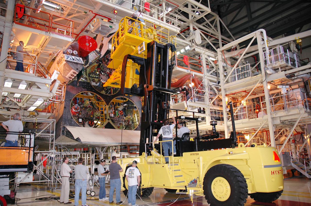KENNEDY SPACE CENTER, FLA. - In the Orbiter Processing Facility, technicians wait below while a Hyster lift moves the first of three Space Shuttle Main Engines (SSME) into position above for installation on Discovery, the vehicle designated for the Return to Flight mission STS-114. Overall, an SSME weighs approximately 7,000 pounds. An SSME operates at greater temperature extremes than any mechanical system in common use today. The liquid hydrogen fuel is -423 degrees Fahrenheit, the second coldest liquid on Earth. When the hydrogen is burned with liquid oxygen, the temperature in the engine's combustion chamber reaches +6000 degrees Fahrenheit -- that's higher than the boiling point of Iron. The maximum equivalent horsepower developed by the three SSMEs is just over 37 million horsepower. The energy released by the three SSMEs is equivalent to the output of 23 Hoover Dams.