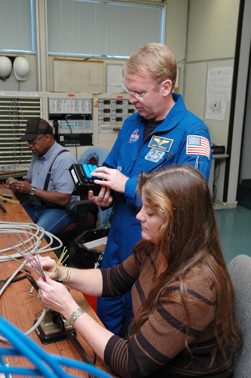 KENNEDY SPACE CENTER, FLA. -  Inside the MILA  Spaceflight Tracking and Data Network Station during a visit to Kennedy, mission STS-114 Mission Specialist Andrew Thomas (center) looks at equipment while Sonja Ashworth, with Honeywell, builds communication cables. The tracking station serves as the primary voice, data and telemetry communications link between the Shuttle and the ground from launch until 7-1_2 minutes into the flight. Millions of clues about the performance of the Space Shuttle’s main engines and other components are communicated to launch managers, technicians and engineers on the ground, who must keep their fingers on the pulse of the Space Shuttle during the critical ascent period. In a typical year, MILA provides through KSC more than 10,000 hours of data between spacecraft and data users.  MILA is also used during a Space Shuttle landing at KSC and provides communications beginning about 13 minutes before touchdown. Also, MILA can be called upon to provide data transfer support for NASA’s Expendable Launch Vehicle missions and orbiting scientific satellites.