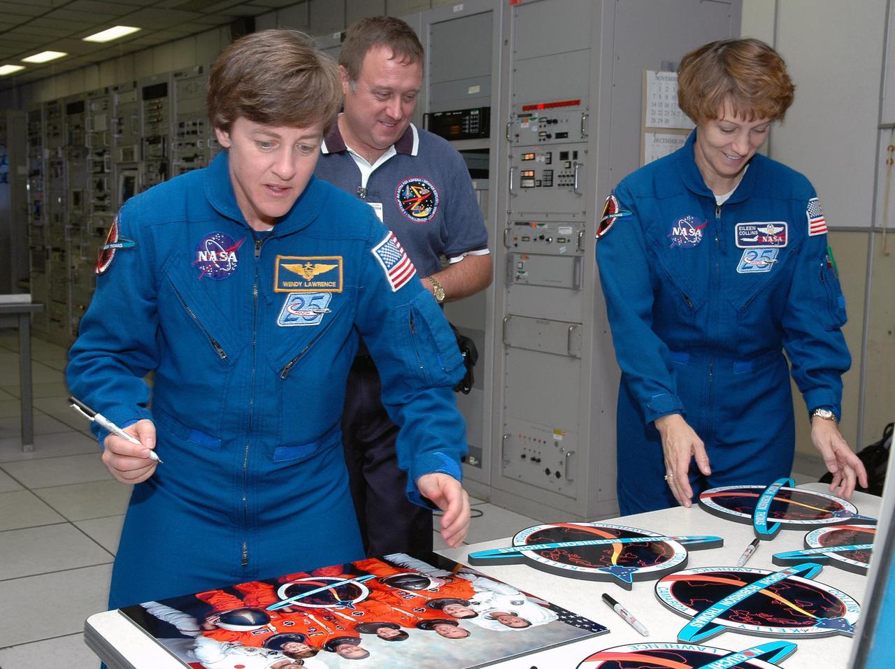 KENNEDY SPACE CENTER, FLA. -  Inside the MILA  Spaceflight Tracking and Data Network Station during a visit to Kennedy, STS-114 Mission Specialist Wendy Lawrence and Commander Eileen Collins sign crew photos and logos.  William Foster, Johnson Space Center ground controller, looks on.  The tracking station serves as the primary voice, data and telemetry communications link between the Shuttle and the ground from launch until 7-1_2 minutes into the flight. Millions of clues about the performance of the Space Shuttle’s main engines and other components are communicated to launch managers, technicians and engineers on the ground, who must keep their fingers on the pulse of the Space Shuttle during the critical ascent period. In a typical year, MILA provides through KSC more than 10,000 hours of data between spacecraft and data users.  MILA is also used during a Space Shuttle landing at KSC and provides communications beginning about 13 minutes before touchdown. Also, MILA can be called upon to provide data transfer support for NASA’s Expendable Launch Vehicle missions and orbiting scientific satellites.