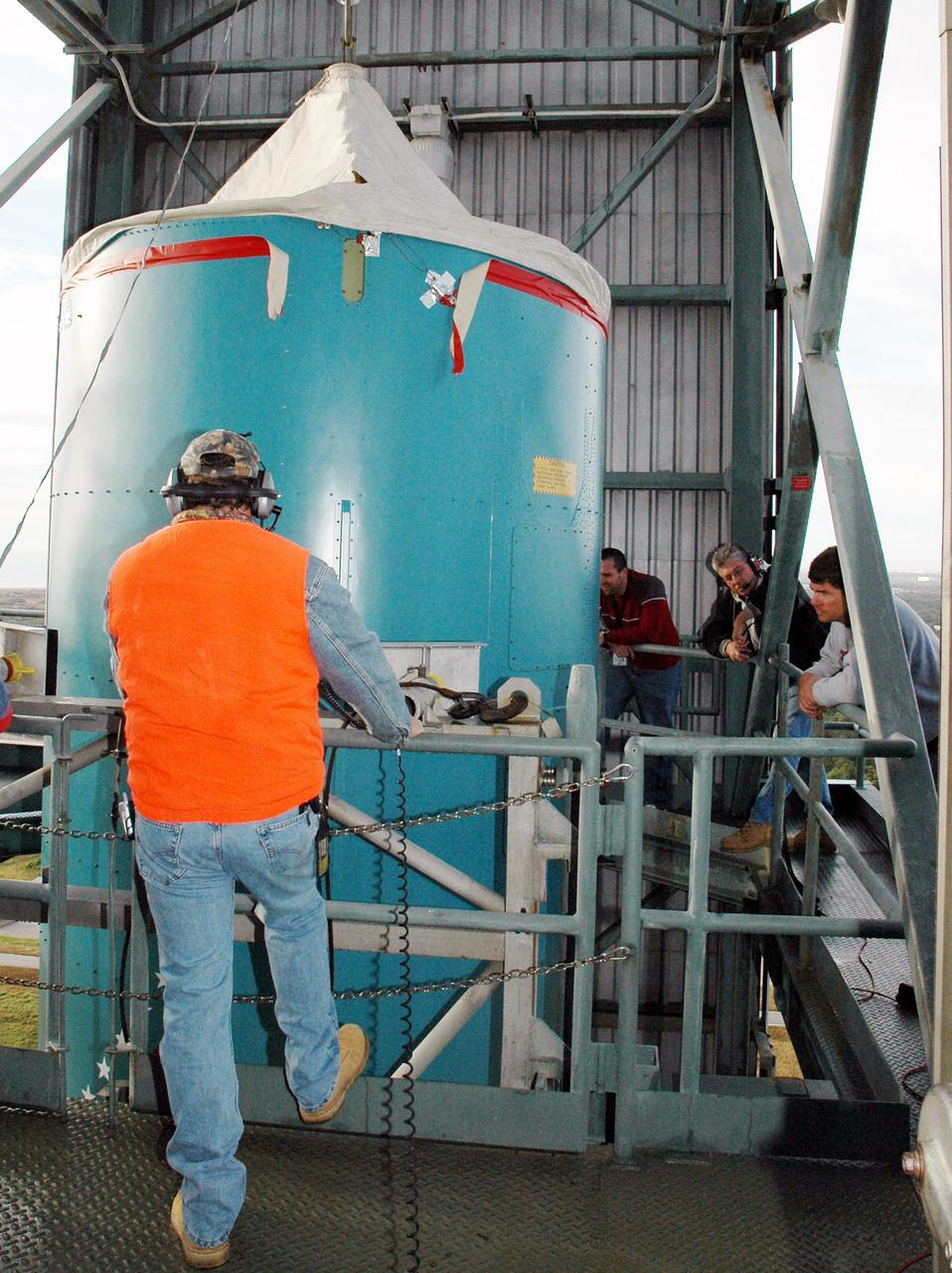KENNEDY SPACE CENTER, FLA. -  On the mobile service tower on Launch Pad 17-B, Cape Canaveral Air Force Station, Fla., Boeing workers stand by as the replacement interstage adapter for the Boeing Delta II is lowered.  Boeing workers will attach the adapter to the rocket’s center body section.  Later the second stage, which was removed to allow access to the previous adapter, will be reattached. The first adapter was removed after it was found to be faulty during a review of launch vehicle hardware. Launch of Deep Impact is now scheduled no earlier than Jan. 12.
